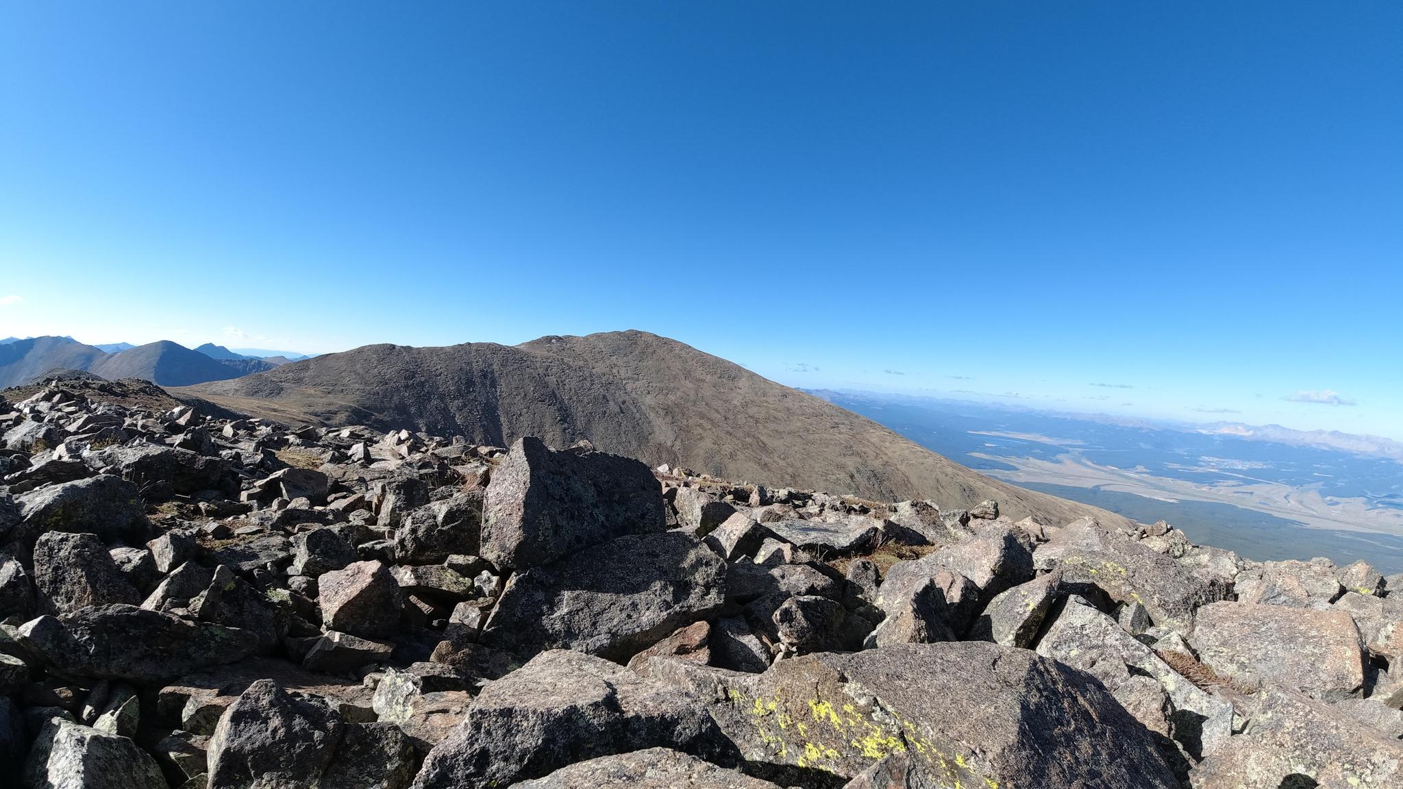 Panoramic view from a rocky mountain summit under a clear, deep blue sky.