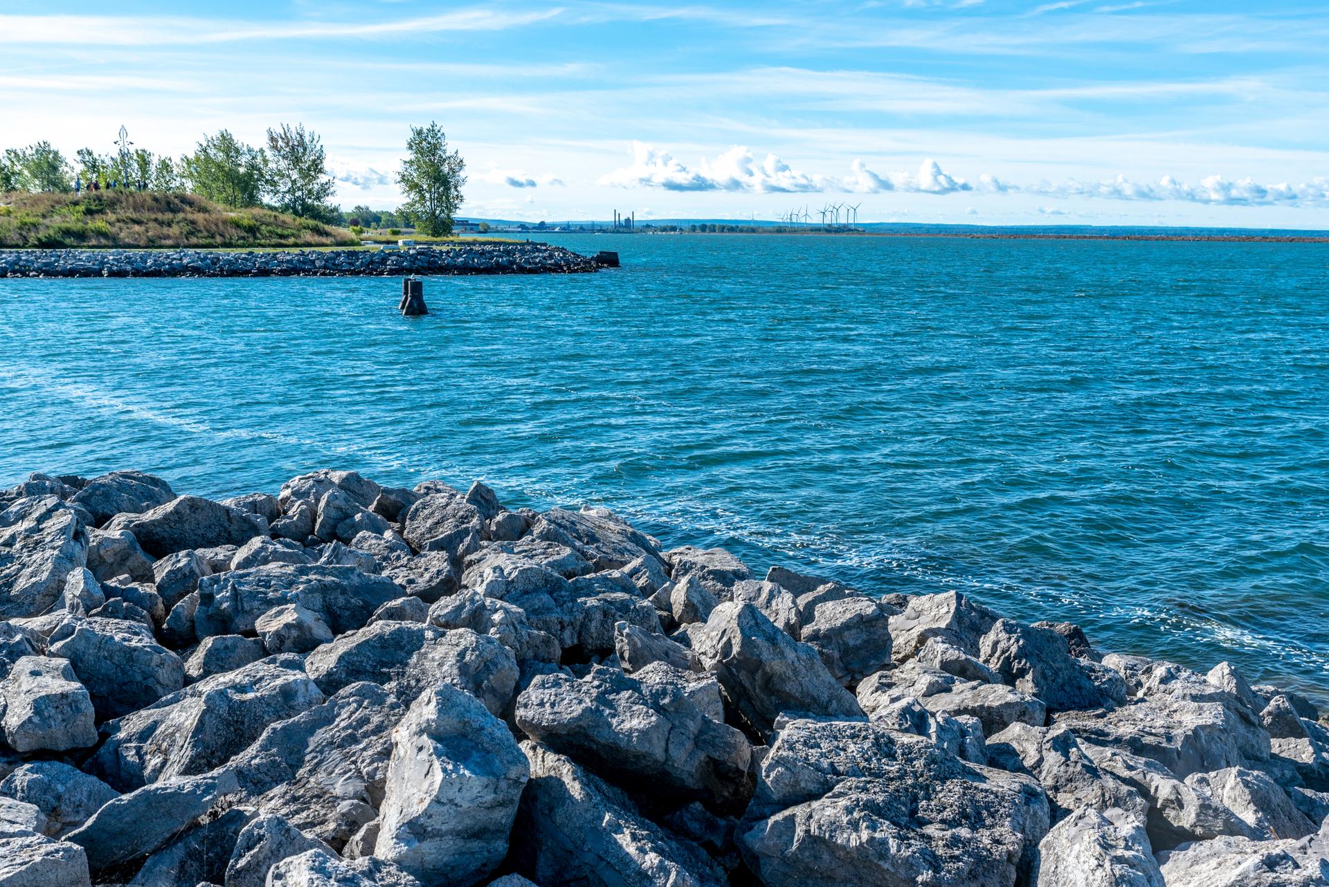 Bright sunny day over a rocky shoreline and calm blue water.