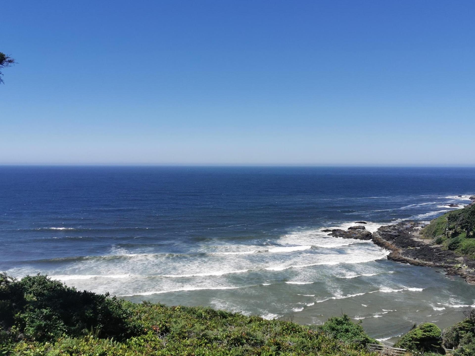 Expansive blue ocean with white waves crashing against a rocky coastline.