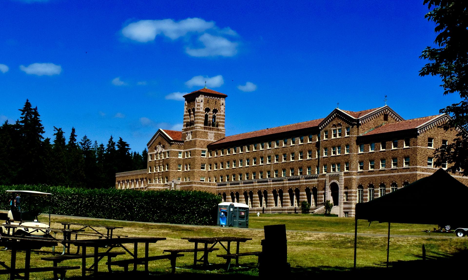 Large brick building with a tower under a bright blue sky, picnic tables.