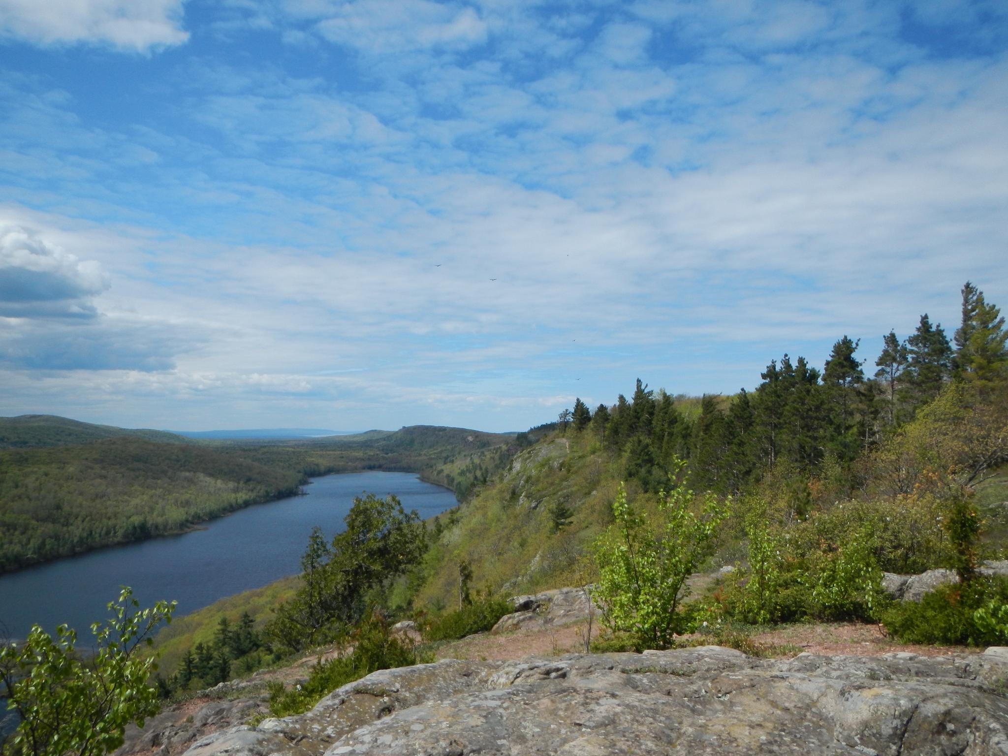 Overlook from a rocky outcrop showing a lake and forested hills under a blue sky.