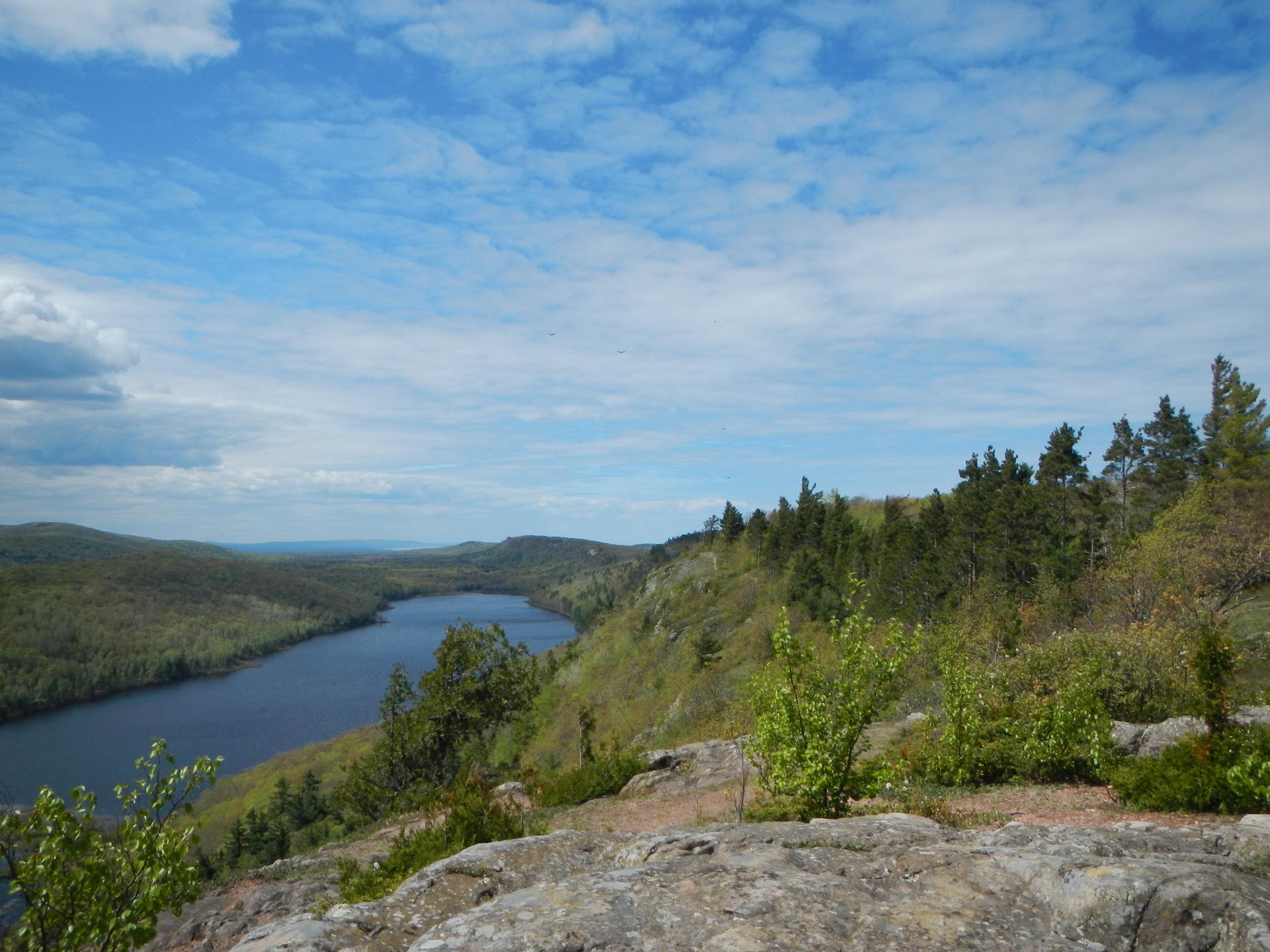 Overlook from a rocky outcrop showing a lake and forested hills under a blue sky.