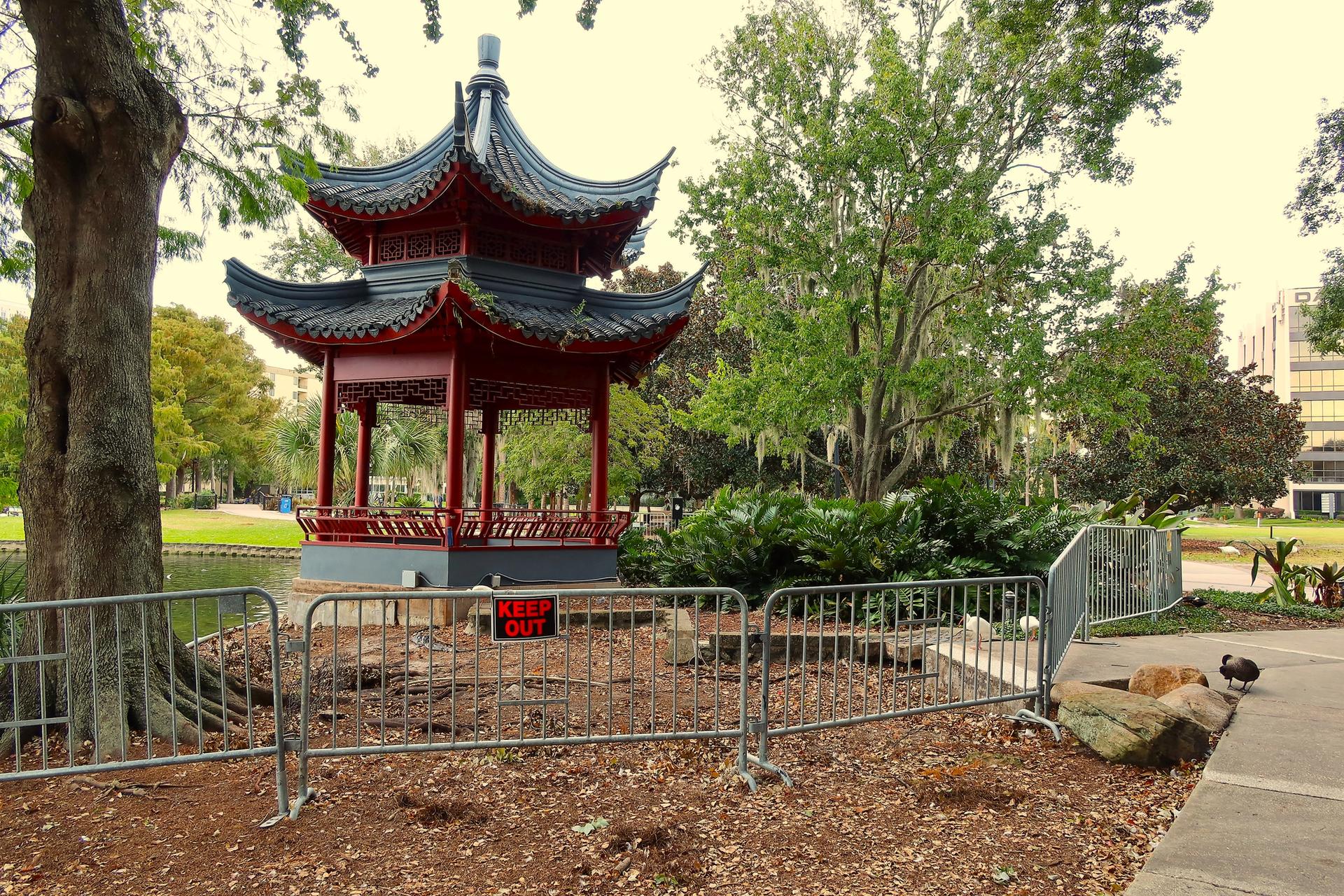 Red pagoda in a park, surrounded by trees and a metal fence.