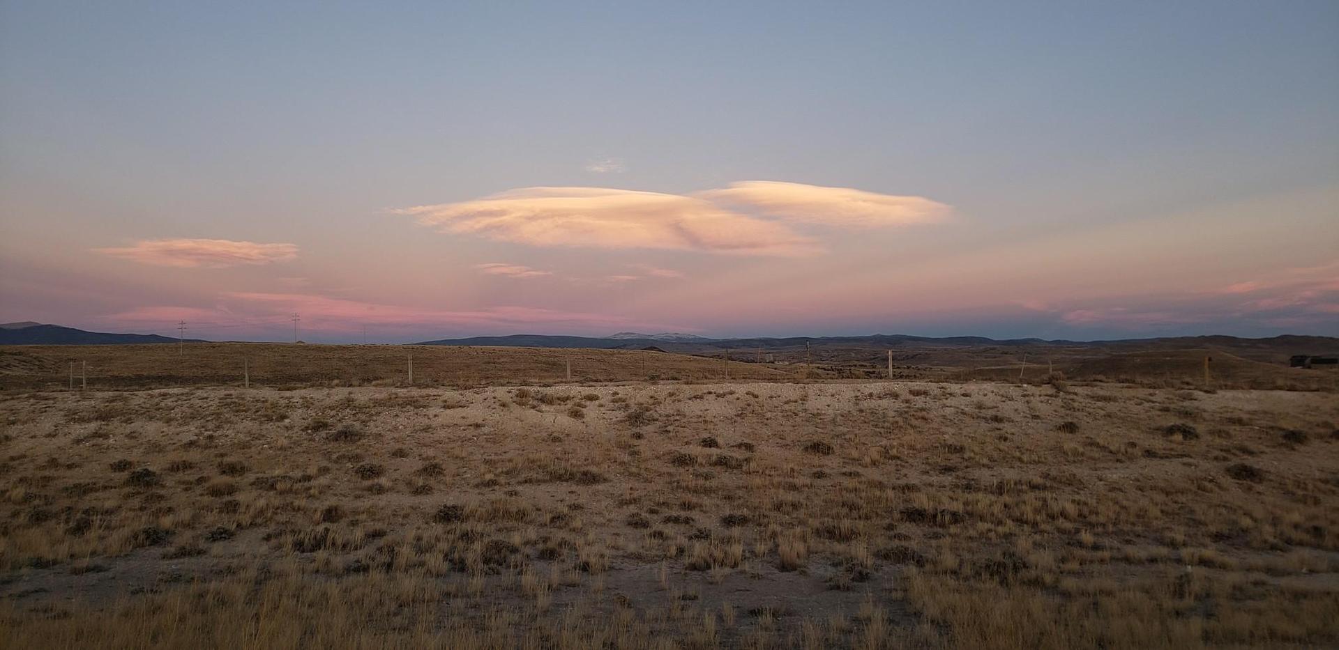 Expansive dry grassland under a dramatic pink and orange sunset sky.