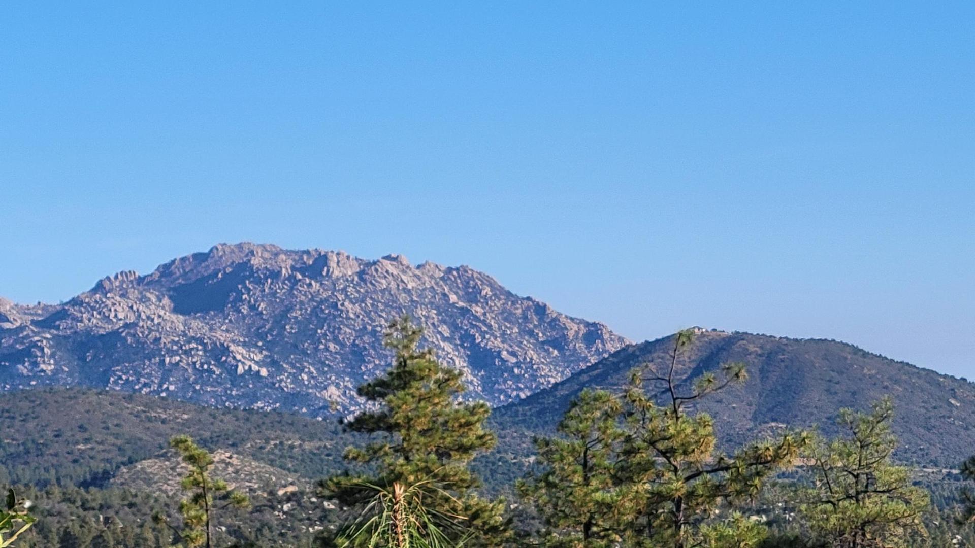 Rocky mountains and forested hills under a clear blue sky.