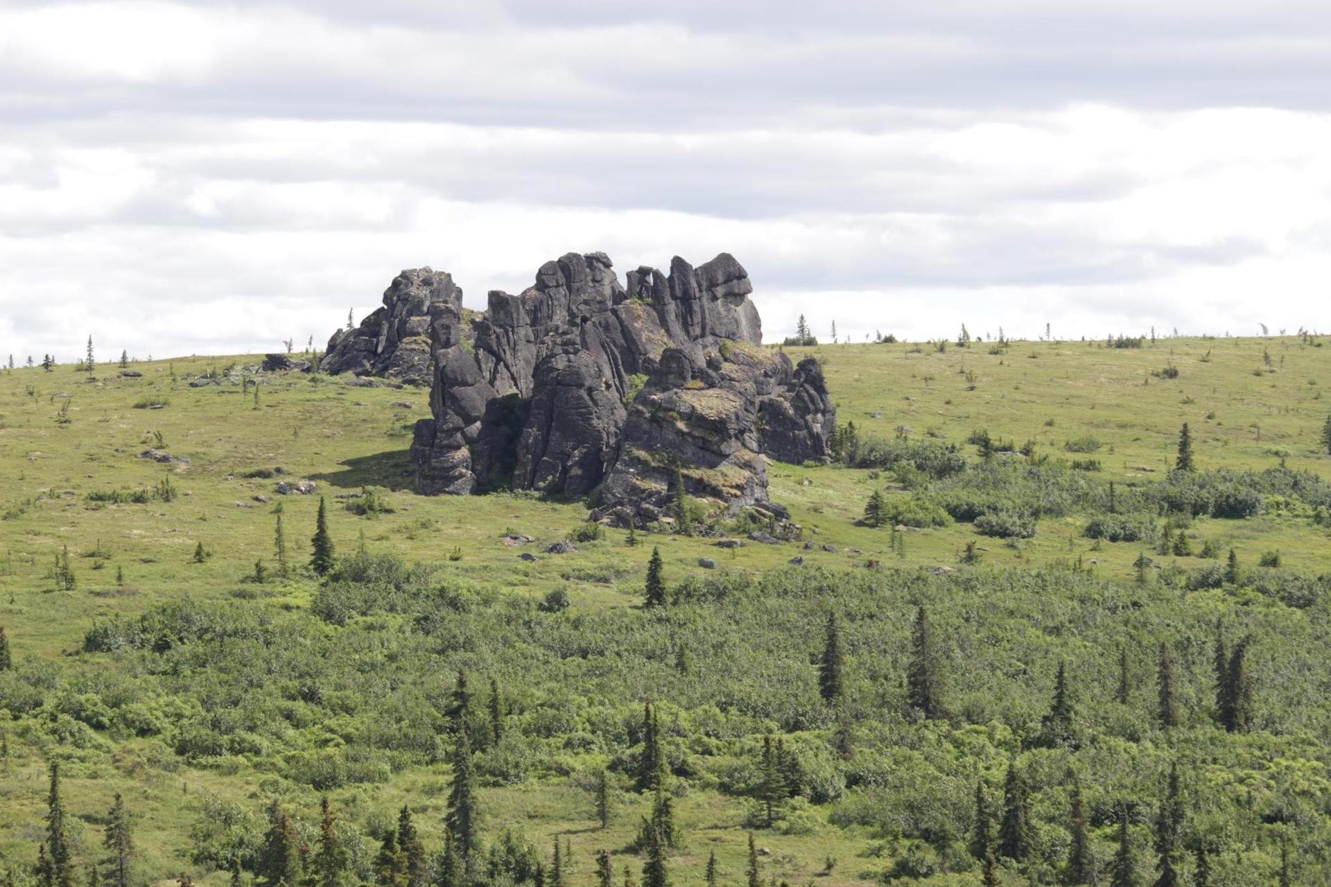 Large rock formations on a green, hilly landscape under a cloudy sky.
