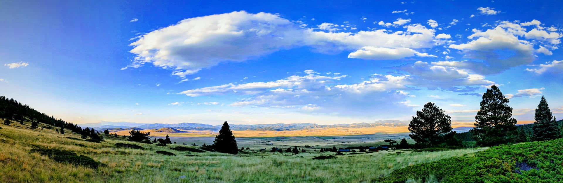Panoramic view of green rolling hills under a bright blue sky with clouds.