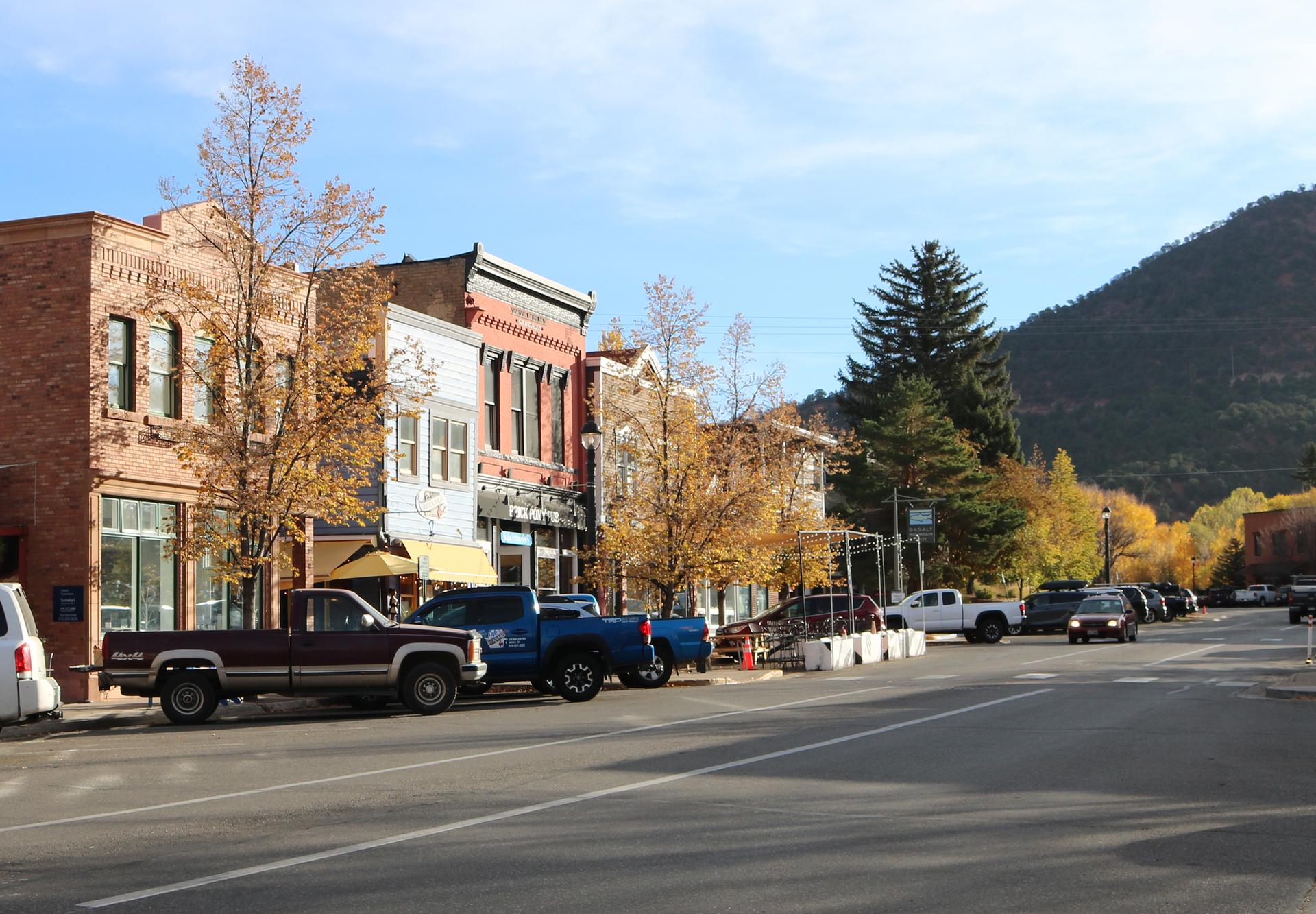 Historic brick buildings line a street with parked cars and autumn trees.