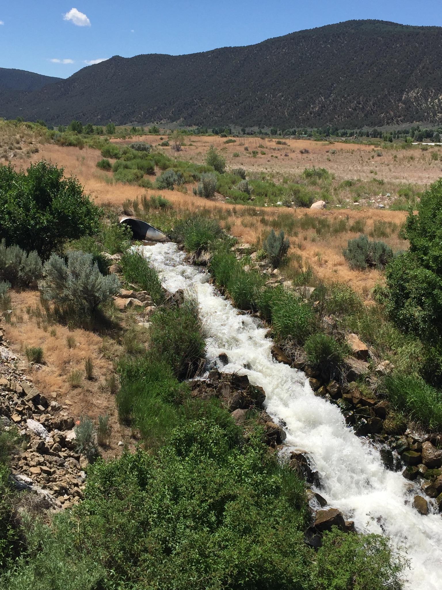 Rushing water flows down a rocky stream bed through dry hills.