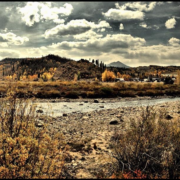 Dramatic cloudy sky over a rocky riverbed and autumn-colored hills.