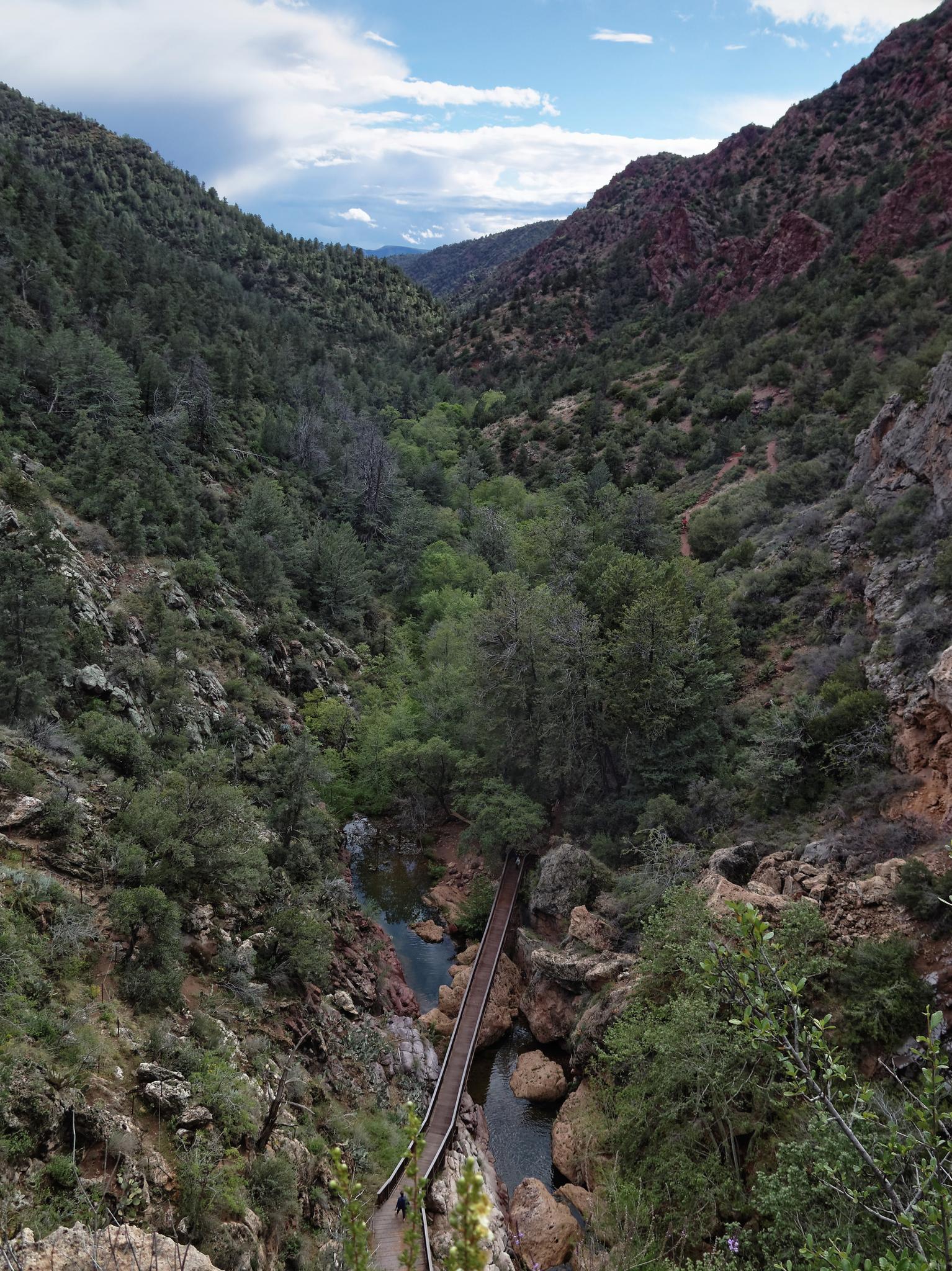 Scenic canyon view with a long bridge over a river, partly cloudy sky.