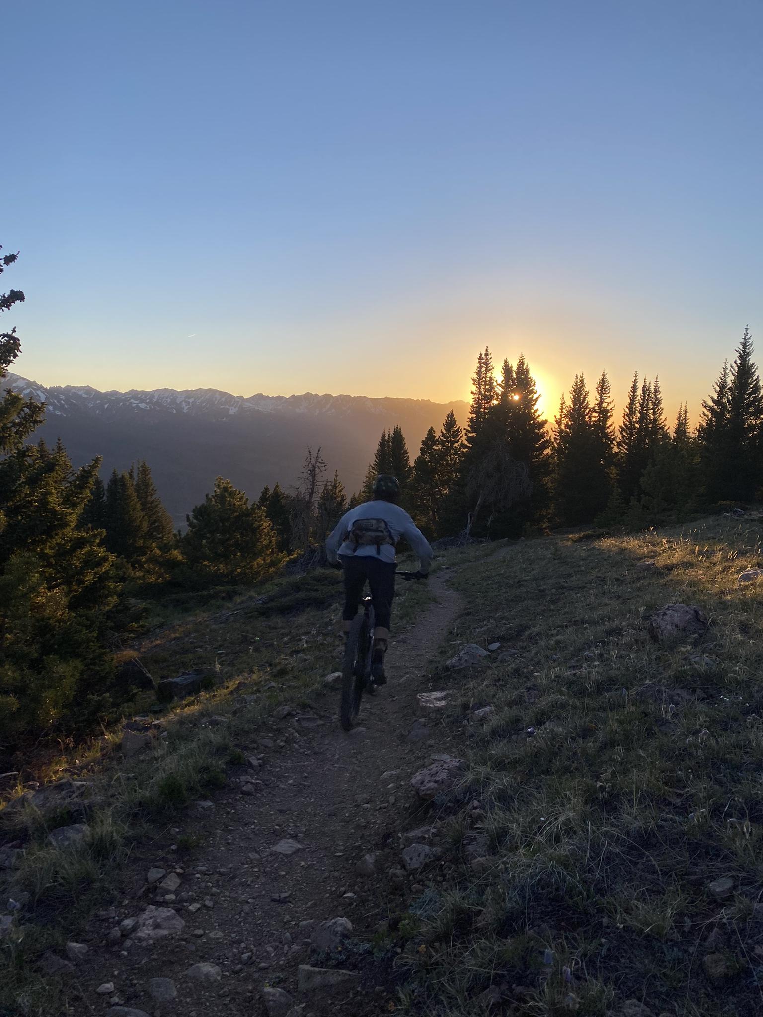 Person mountain biking on a dirt trail during a golden sunset.