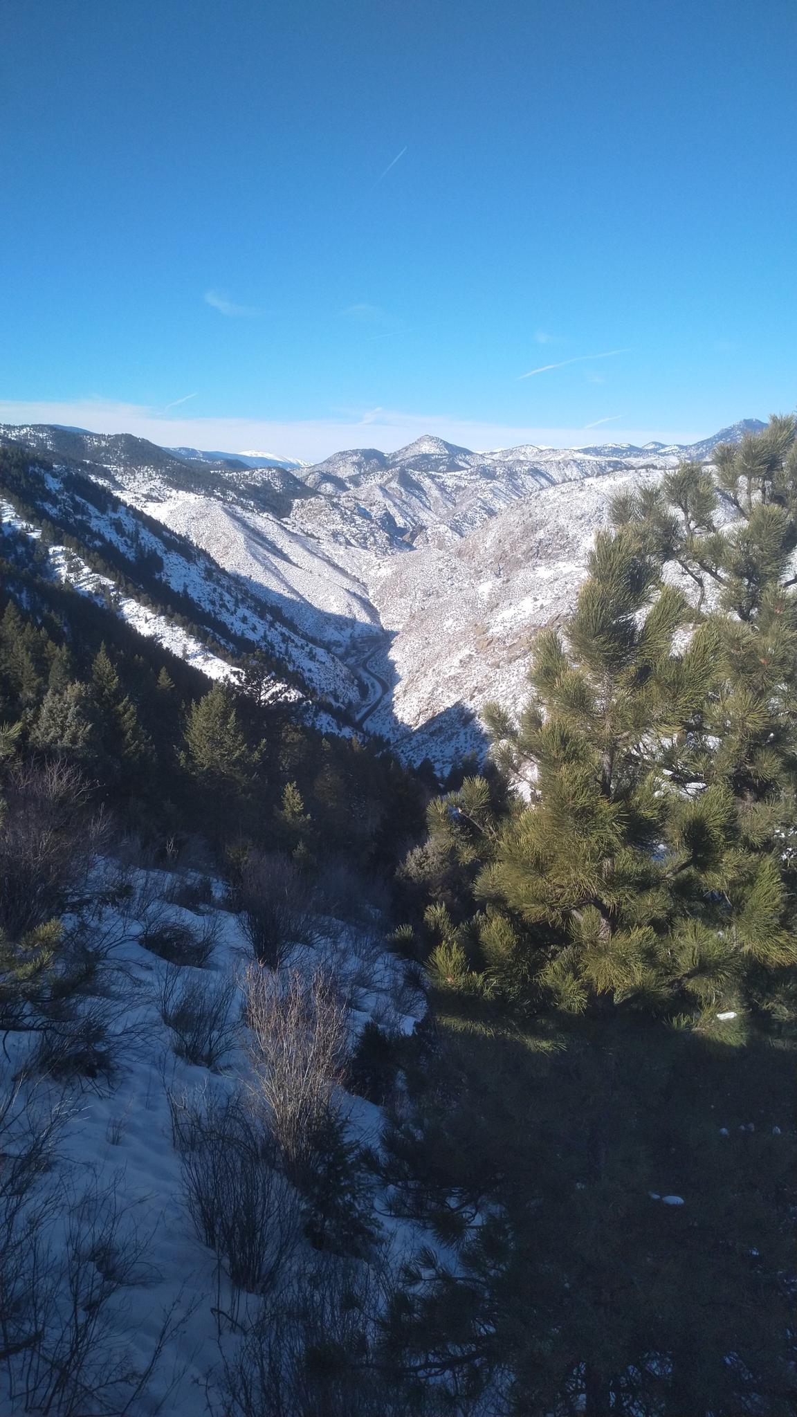 A deep, snow-dusted valley surrounded by mountains under a clear blue sky.