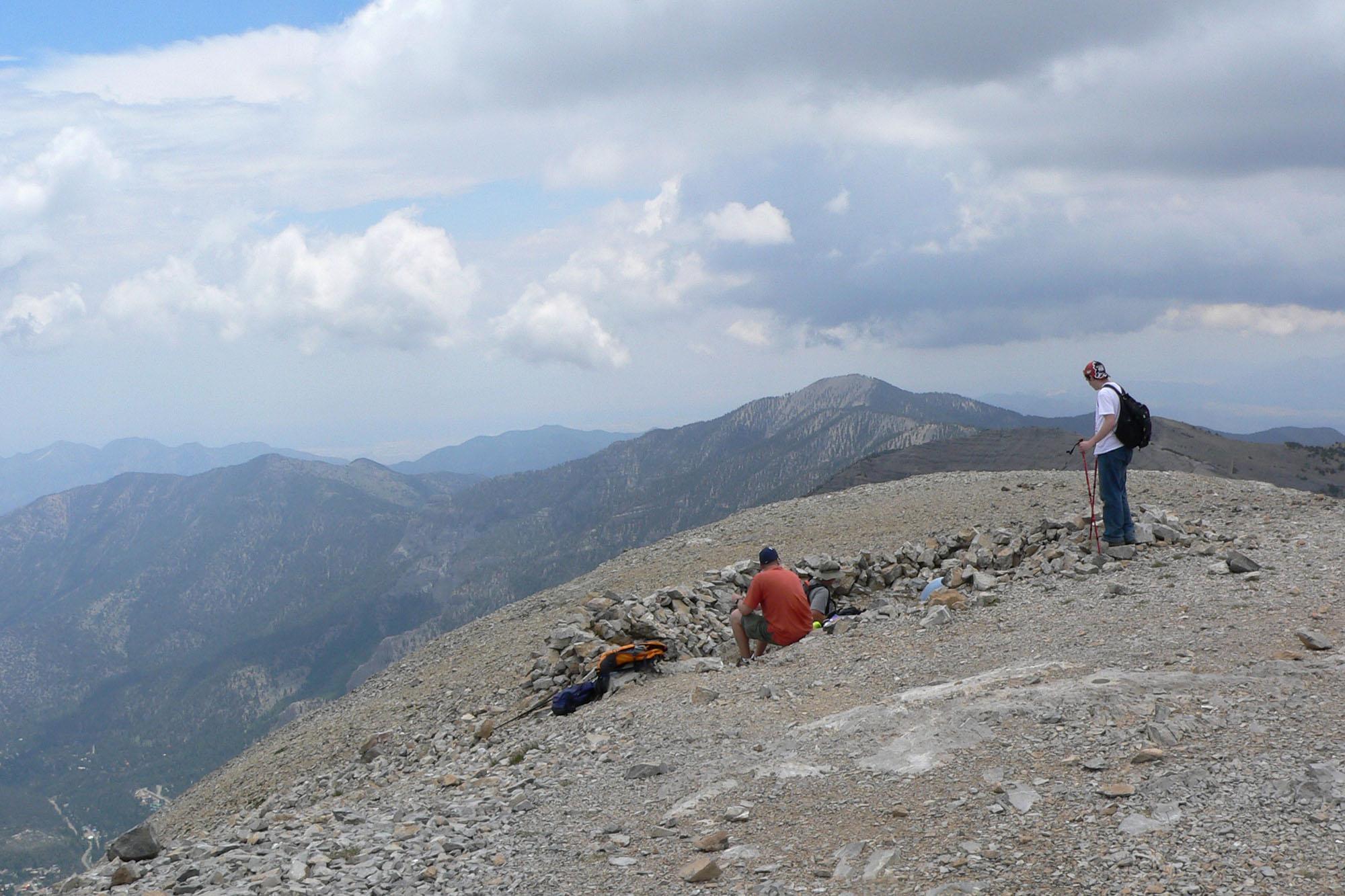 Two hikers resting on a rocky mountain ridge with distant peaks.