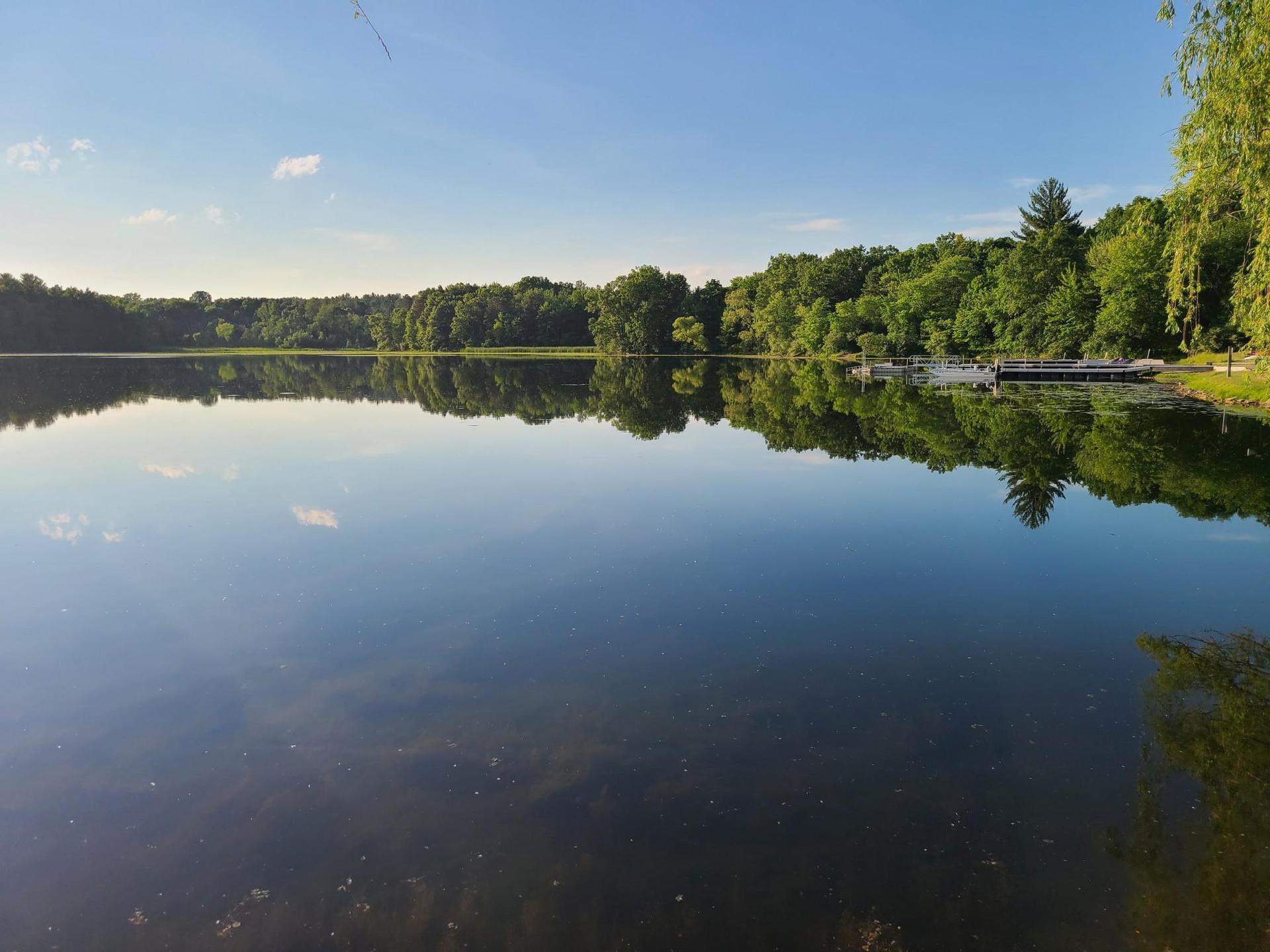 Calm lake reflecting blue sky and green trees on a bright sunny day.