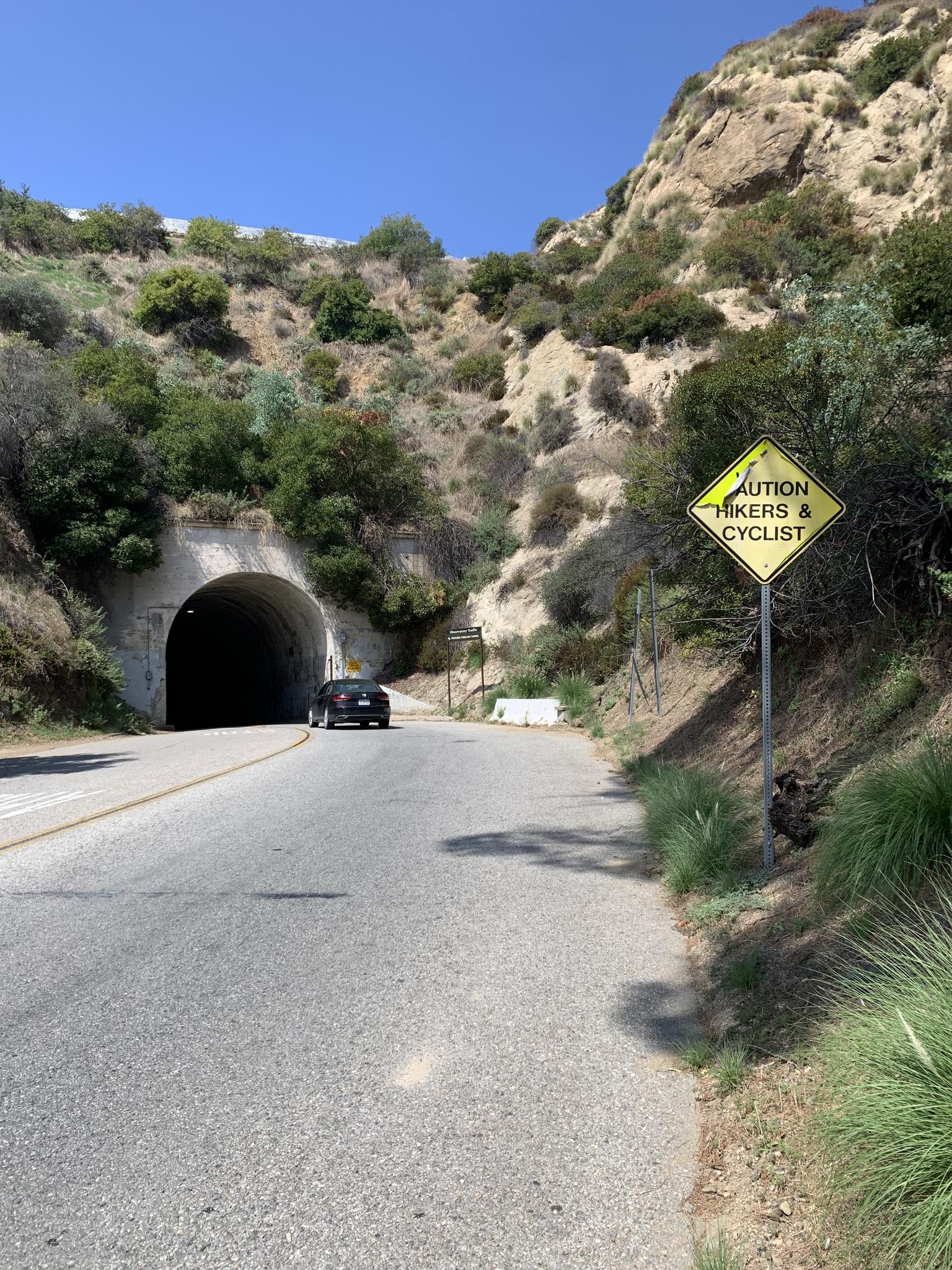 Road leading to a dark tunnel entrance, with a caution sign.