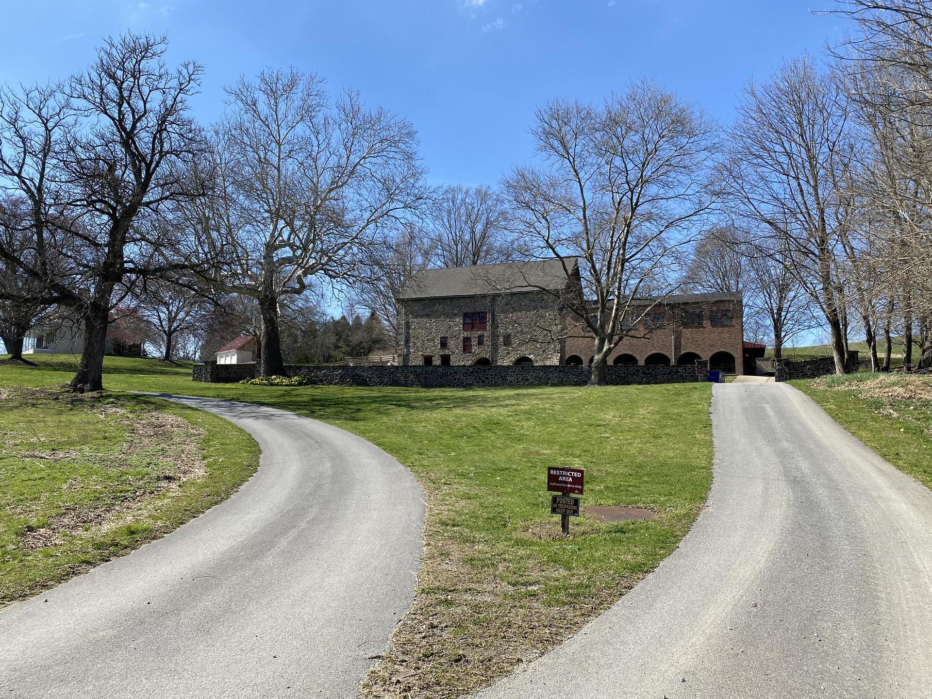 Stone building on a grassy hill with bare trees under a clear sky.