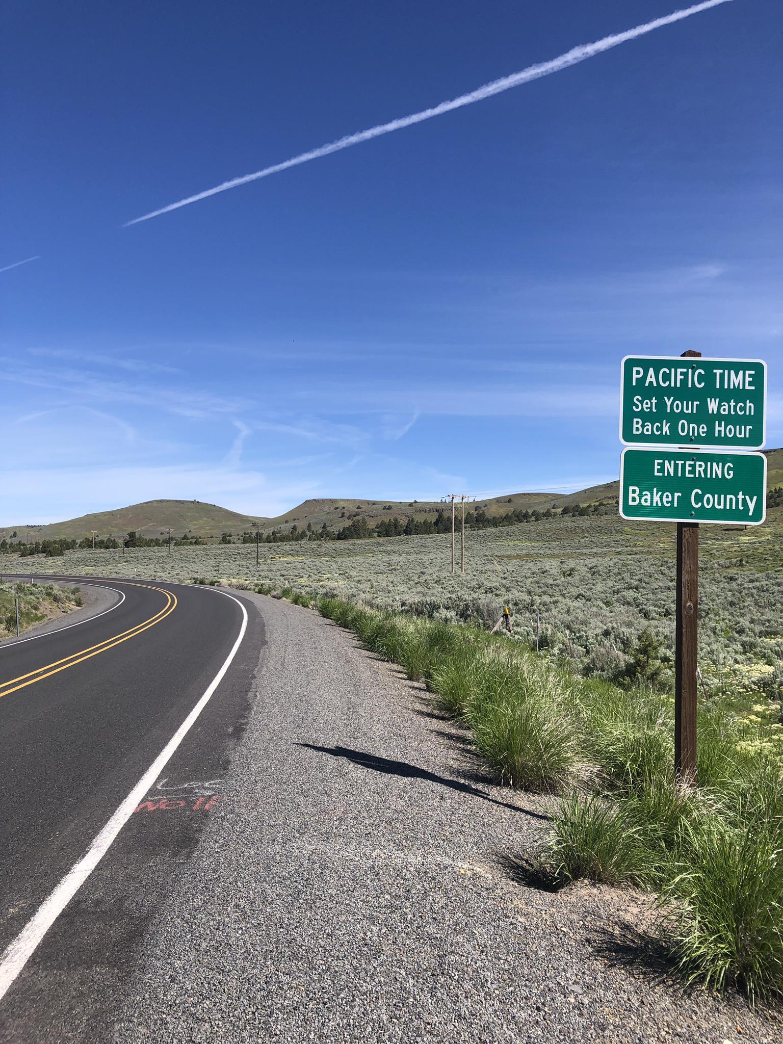 Paved road curves left past a green sign in a dry, hilly landscape.