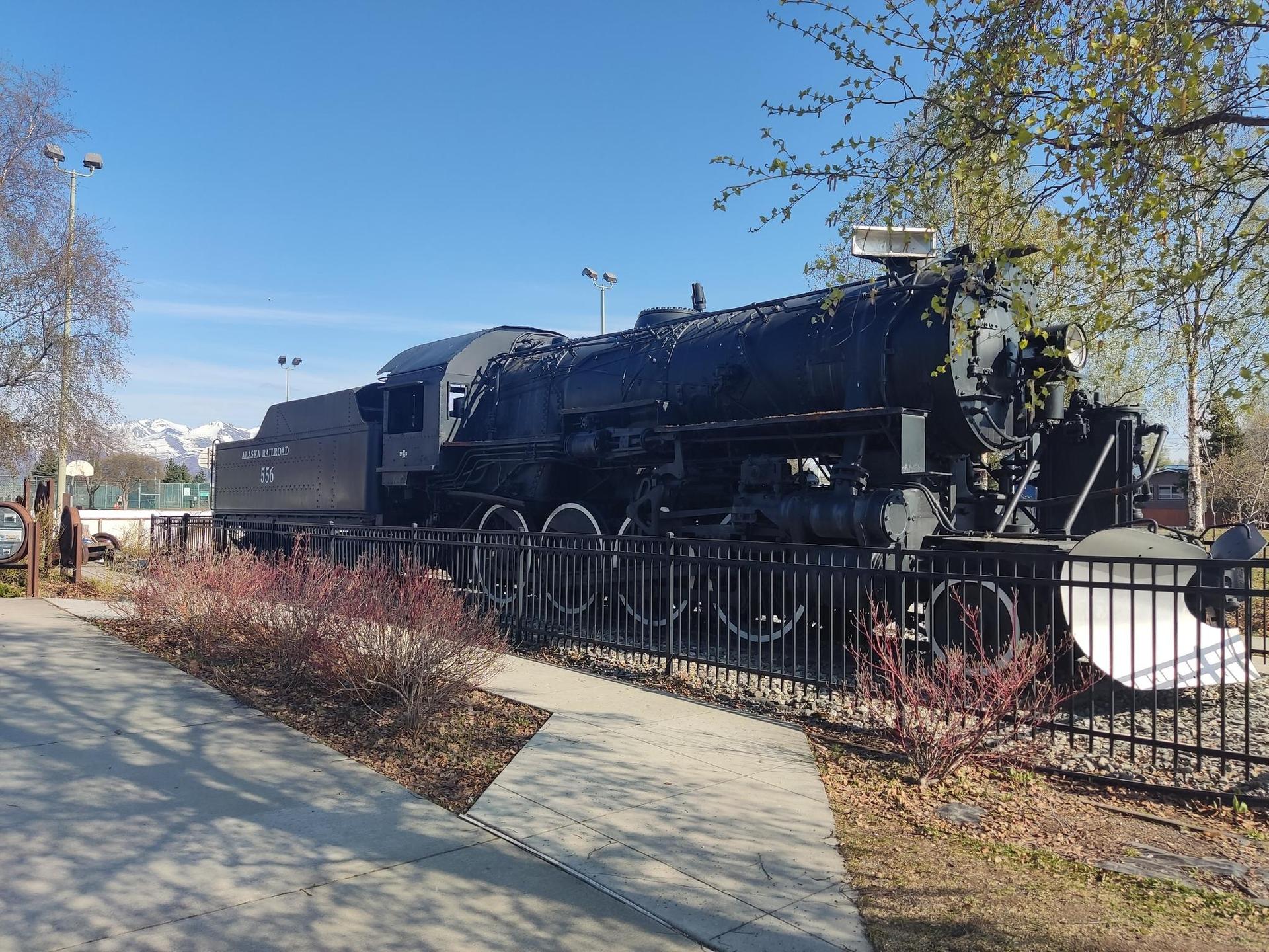 Historic black steam locomotive on display outdoors under a bright blue sky.
