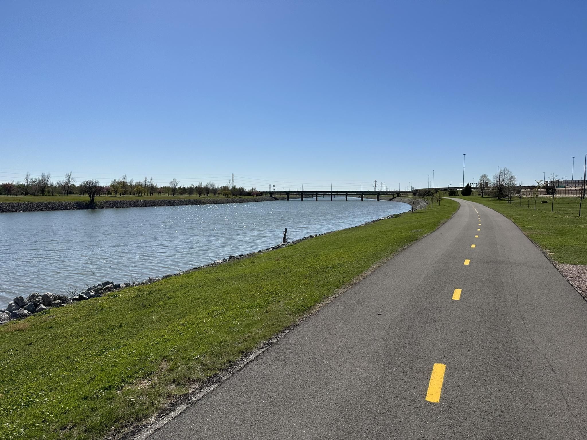 Paved path alongside a river under a clear blue sky. - Oklahoma River Trail Loop