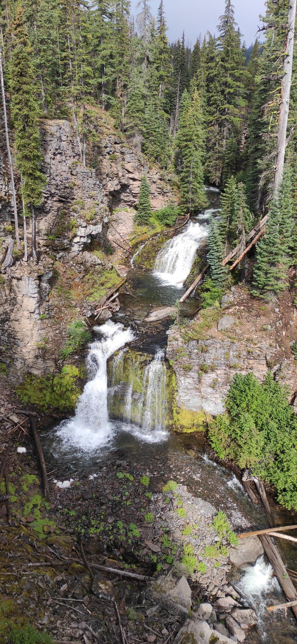 Multi-tiered waterfall cascades down a rocky, forested canyon under diffused light.
