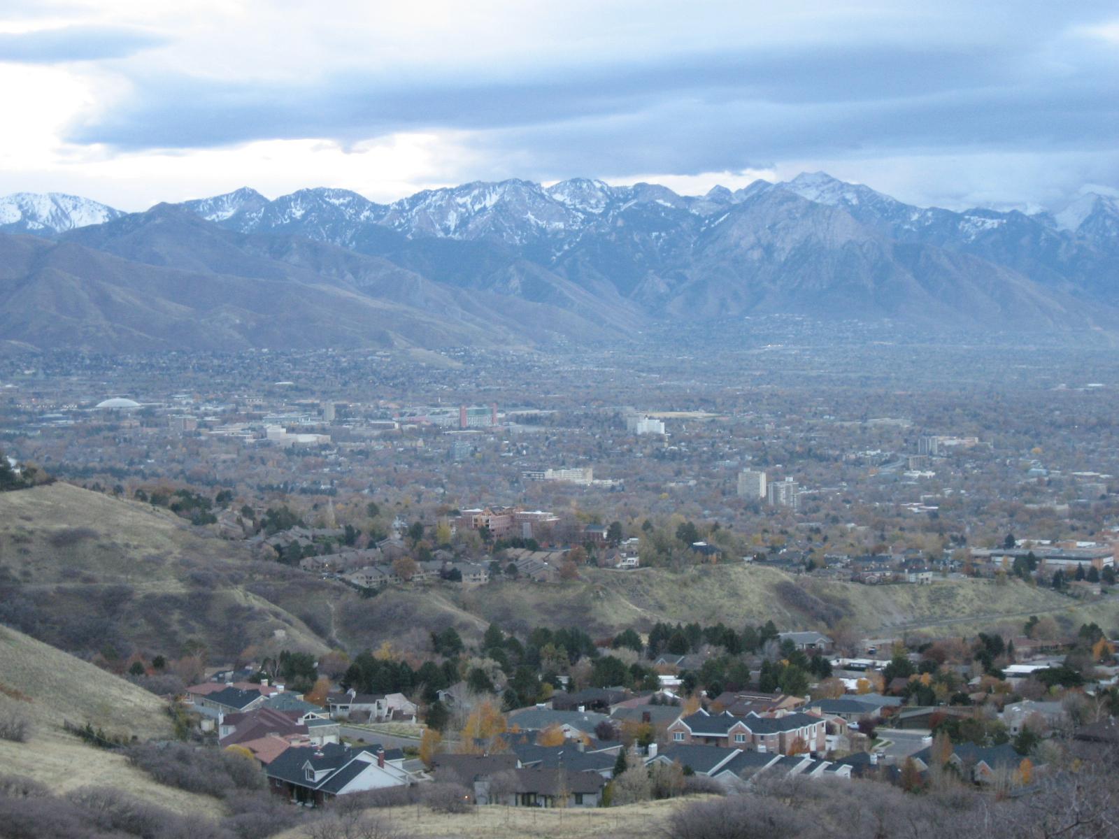 Overcast view of a city and houses nestled below large snow-capped mountains.
