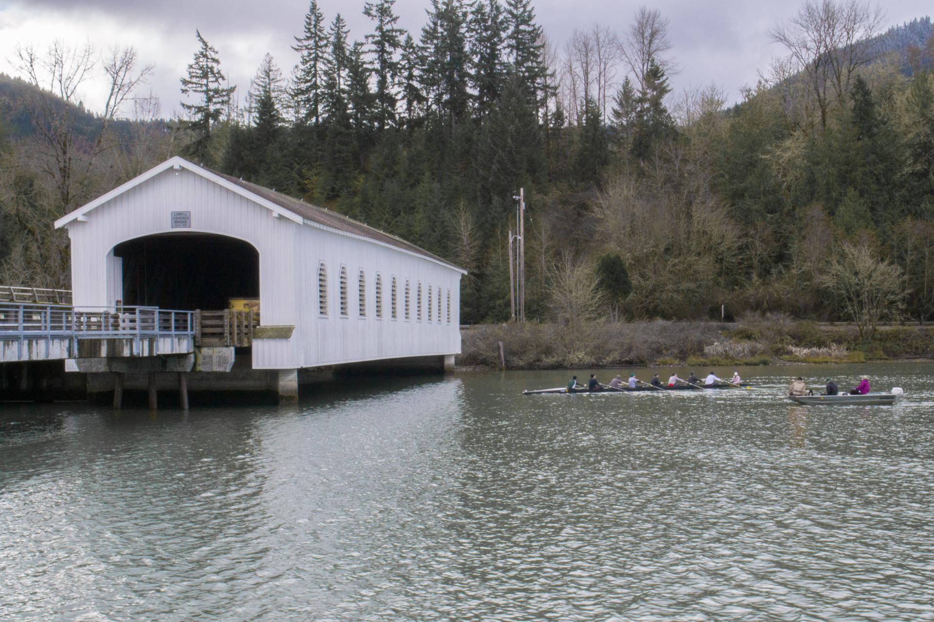 White covered bridge over a river with people rowing, under an overcast sky.
