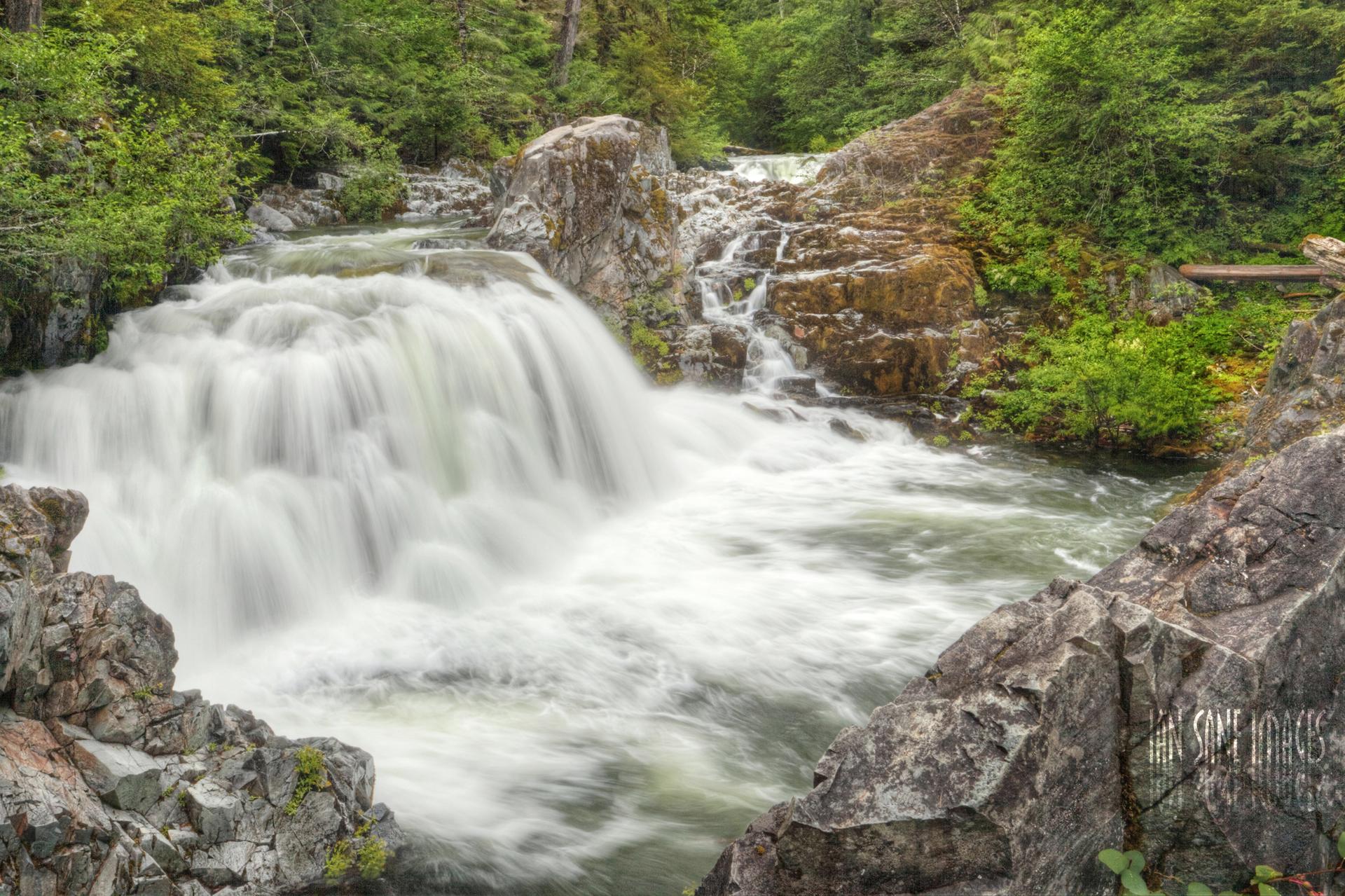 Powerful waterfall cascades over rocks in a lush green forest.