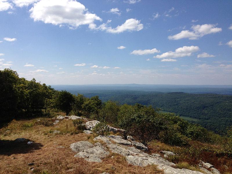 Sunny panoramic view of green forested hills from a rocky mountain top.