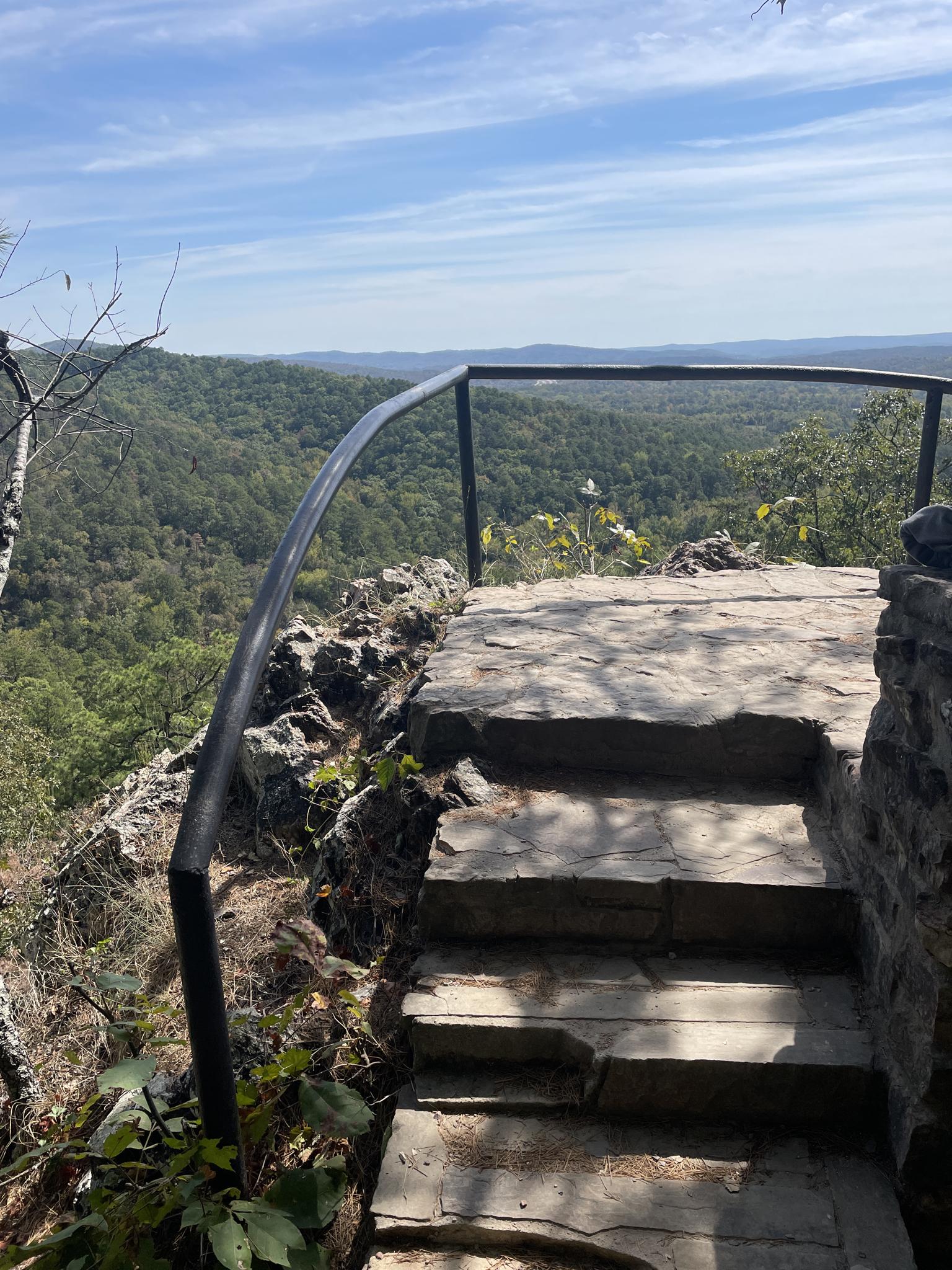 Stone steps and railing overlooking a vast green forested valley.