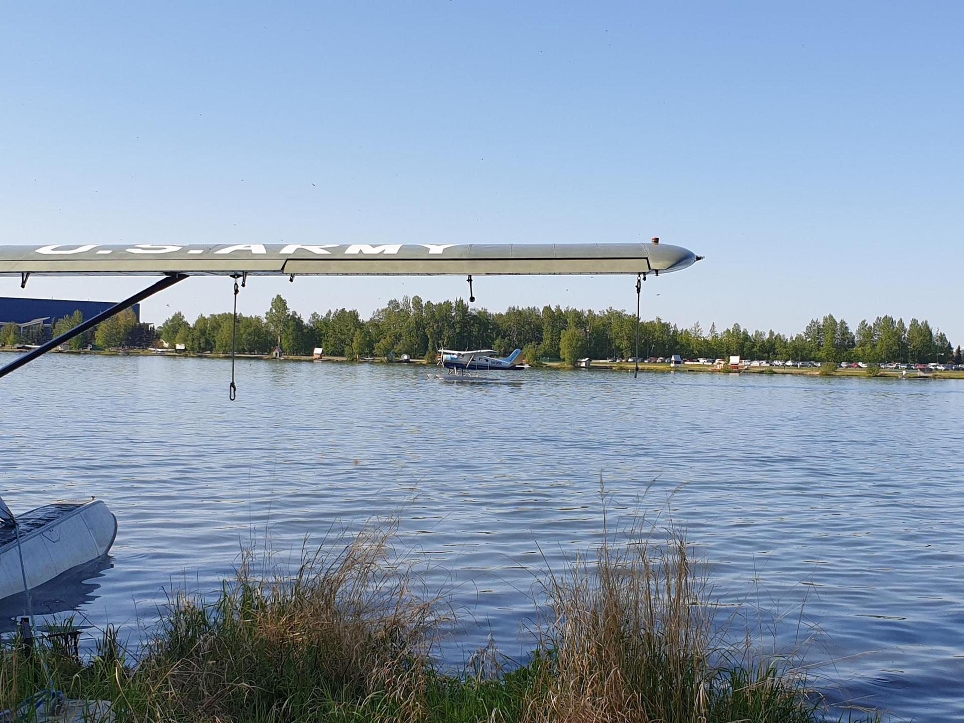 A floatplane wing extends over a calm lake with a distant treeline.