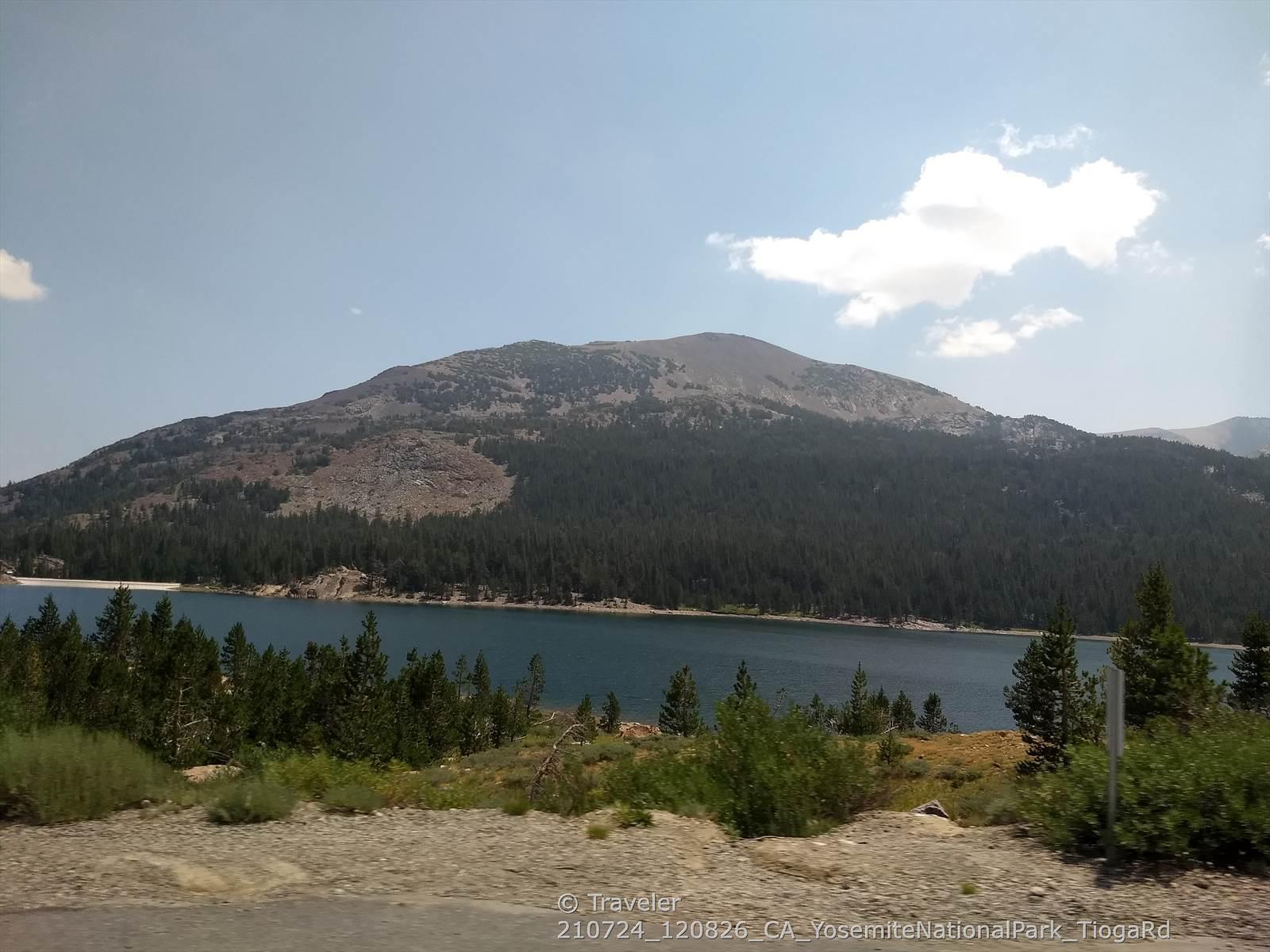 Expansive lake with forested shores and a large mountain under a partly cloudy sky.