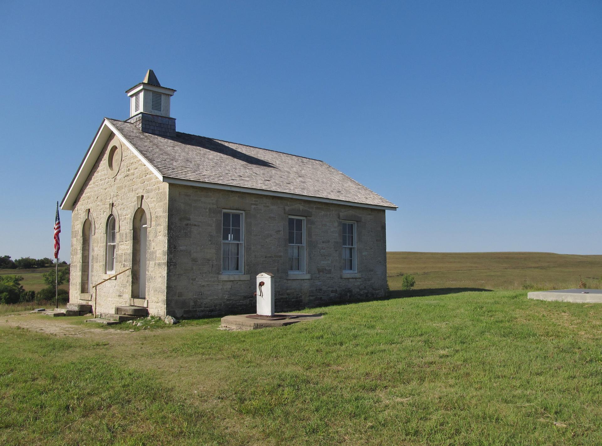 Old stone building with a cupola in a sunny, grassy field.