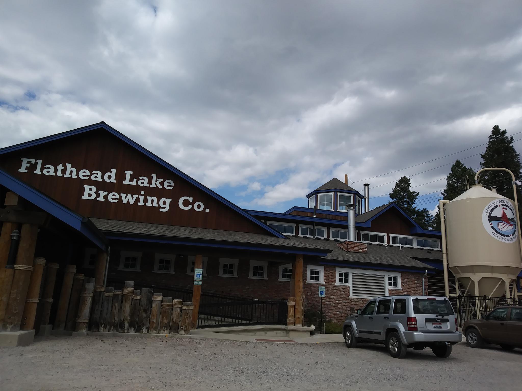 A large brewery building with parked cars under a cloudy sky.