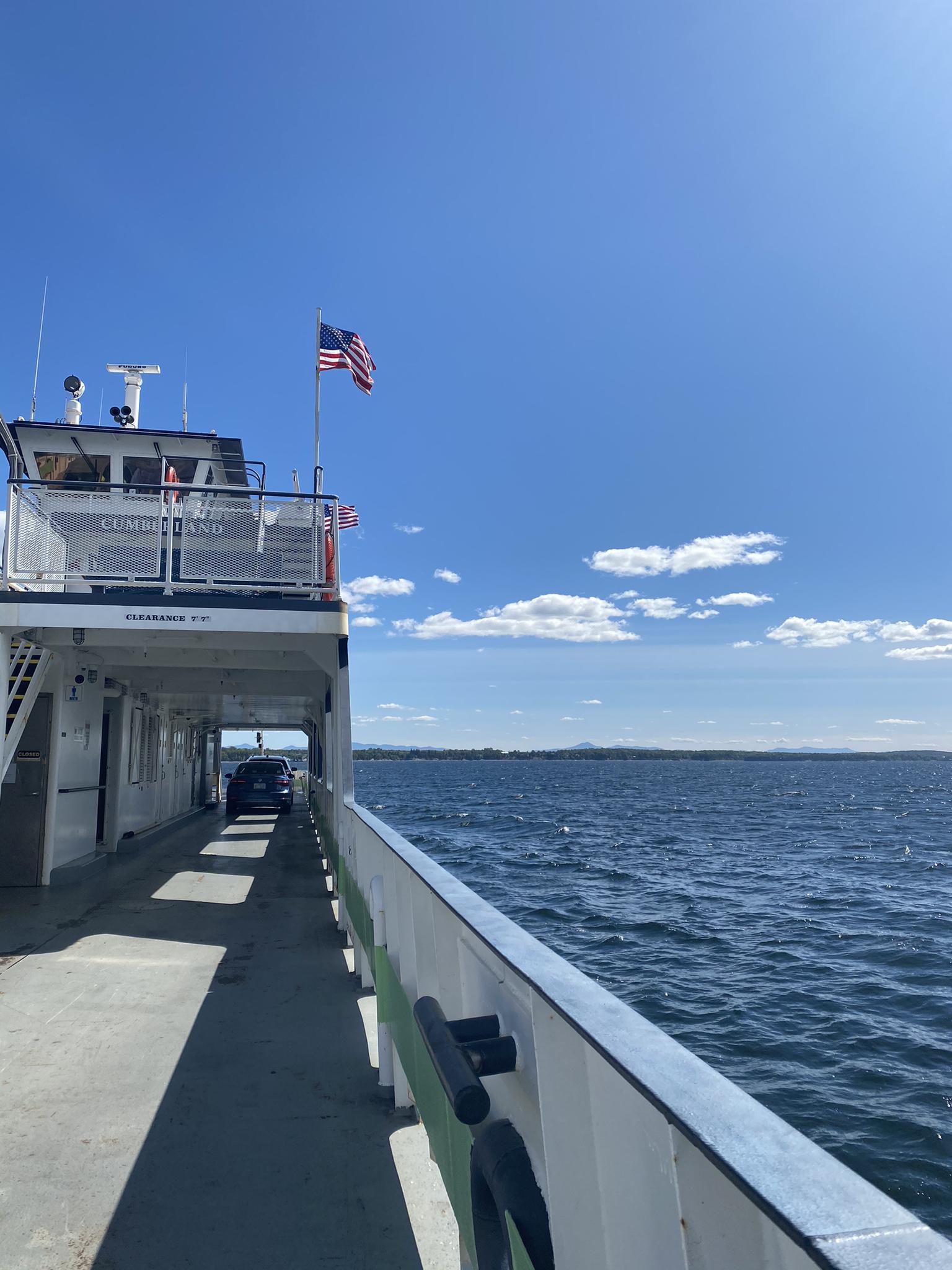 Ferry boat deck with an American flag sailing on bright, open water.