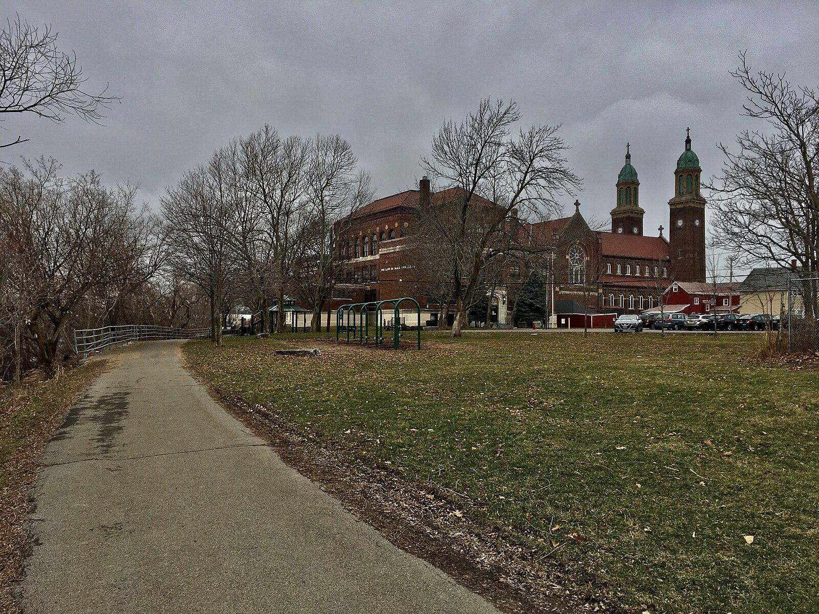 Paved path next to a grassy field, leading to a large brick building.