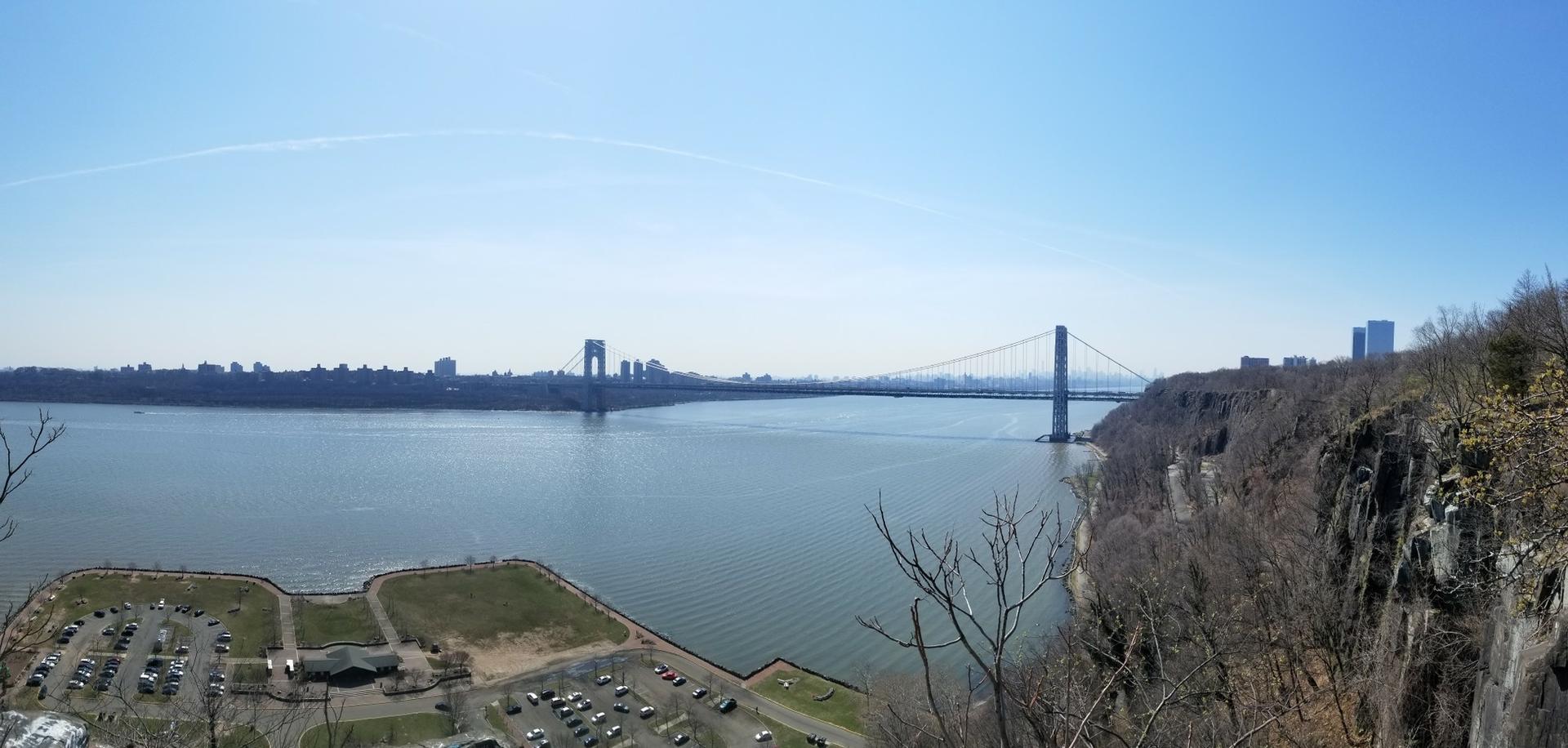 Wide river with a large suspension bridge under a clear blue sky.