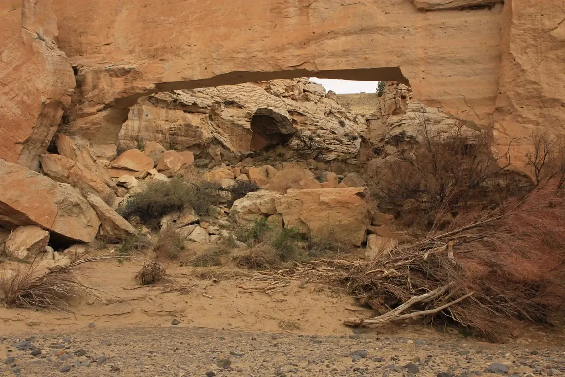 A large natural rock arch spans a dry, rocky desert landscape.