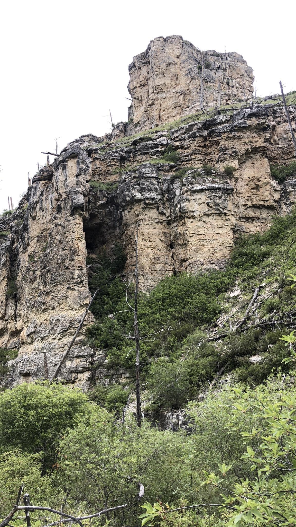A tall, rugged rock formation with a large cave opening on a cloudy day.
