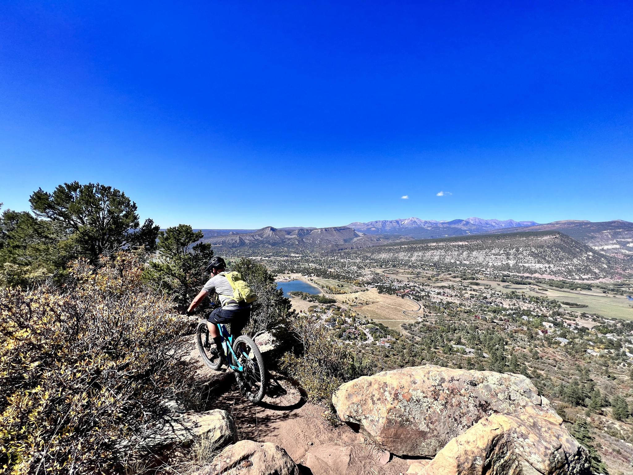 Mountain biker on a rocky trail overlooking a valley and distant mountains.