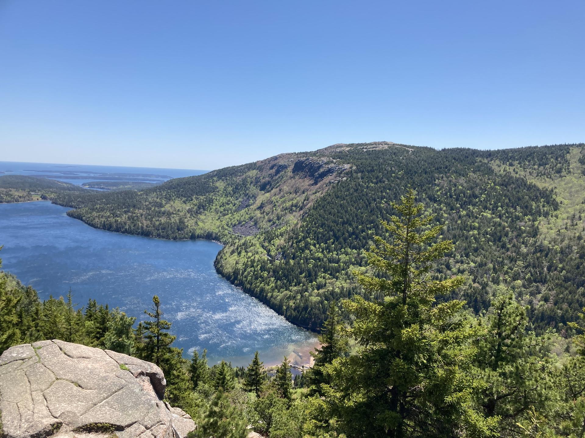 Bright sunny day, panoramic view of a large lake surrounded by lush green forests.