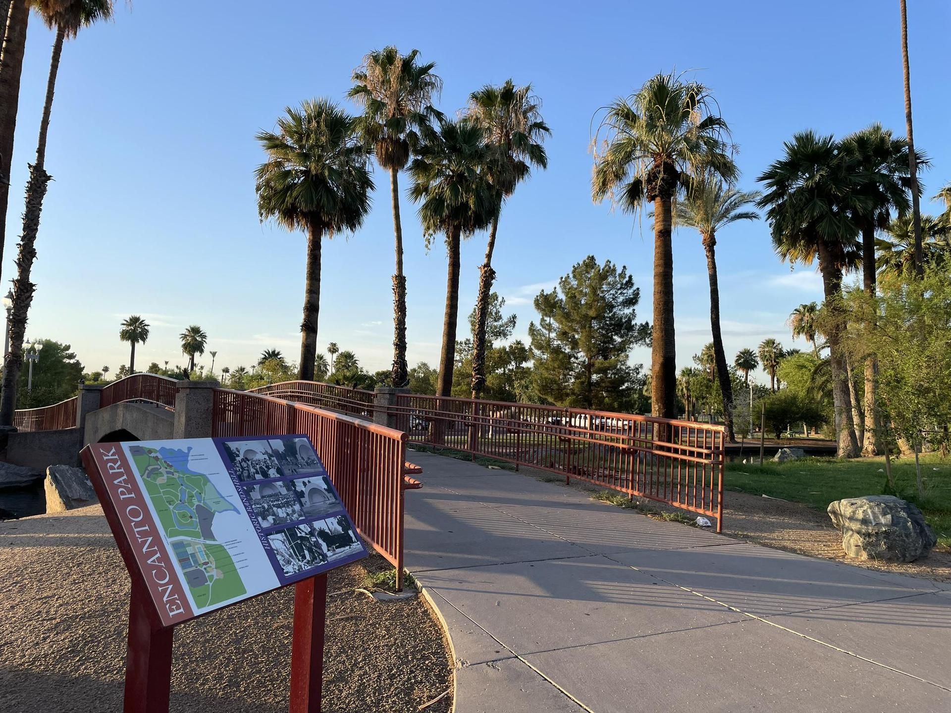 Park sign, paved path, and bridge with palm trees under clear sky.
