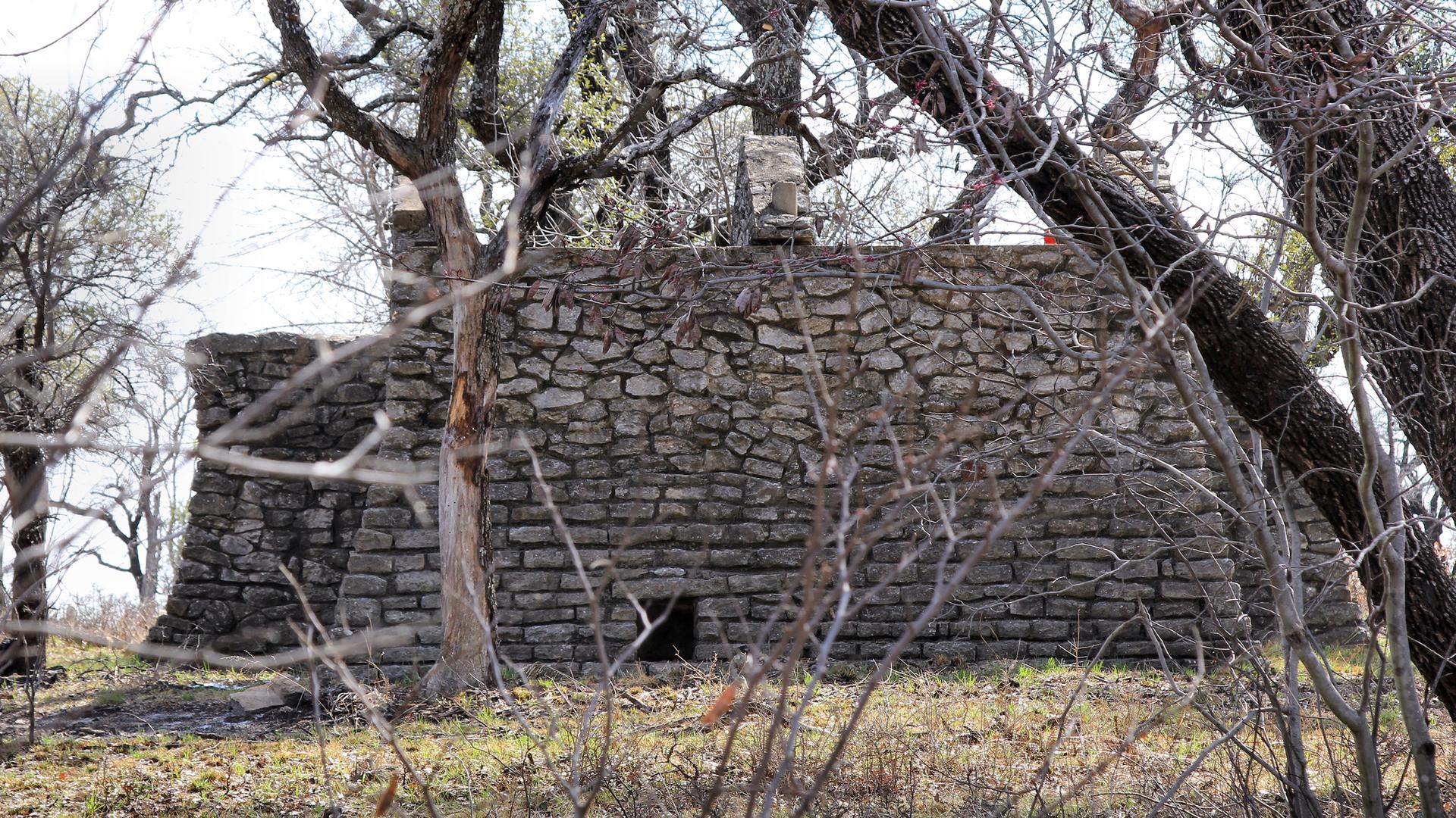An old stone structure with a small opening, surrounded by bare trees.