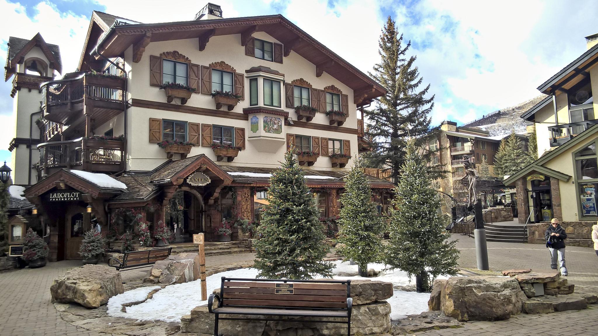 Large building with snow patches, evergreen trees, and a person walking.