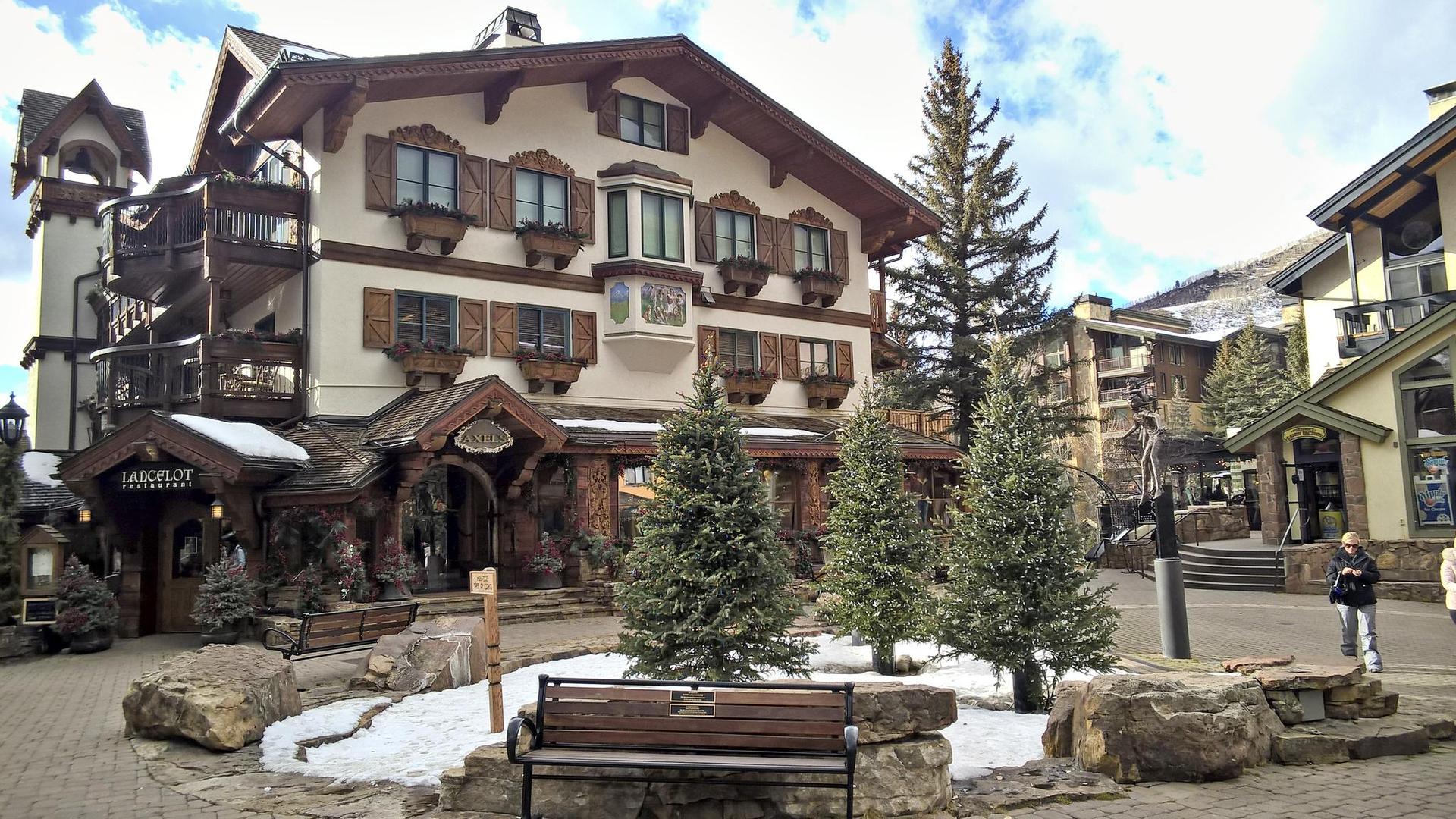 Large building with snow patches, evergreen trees, and a person walking.