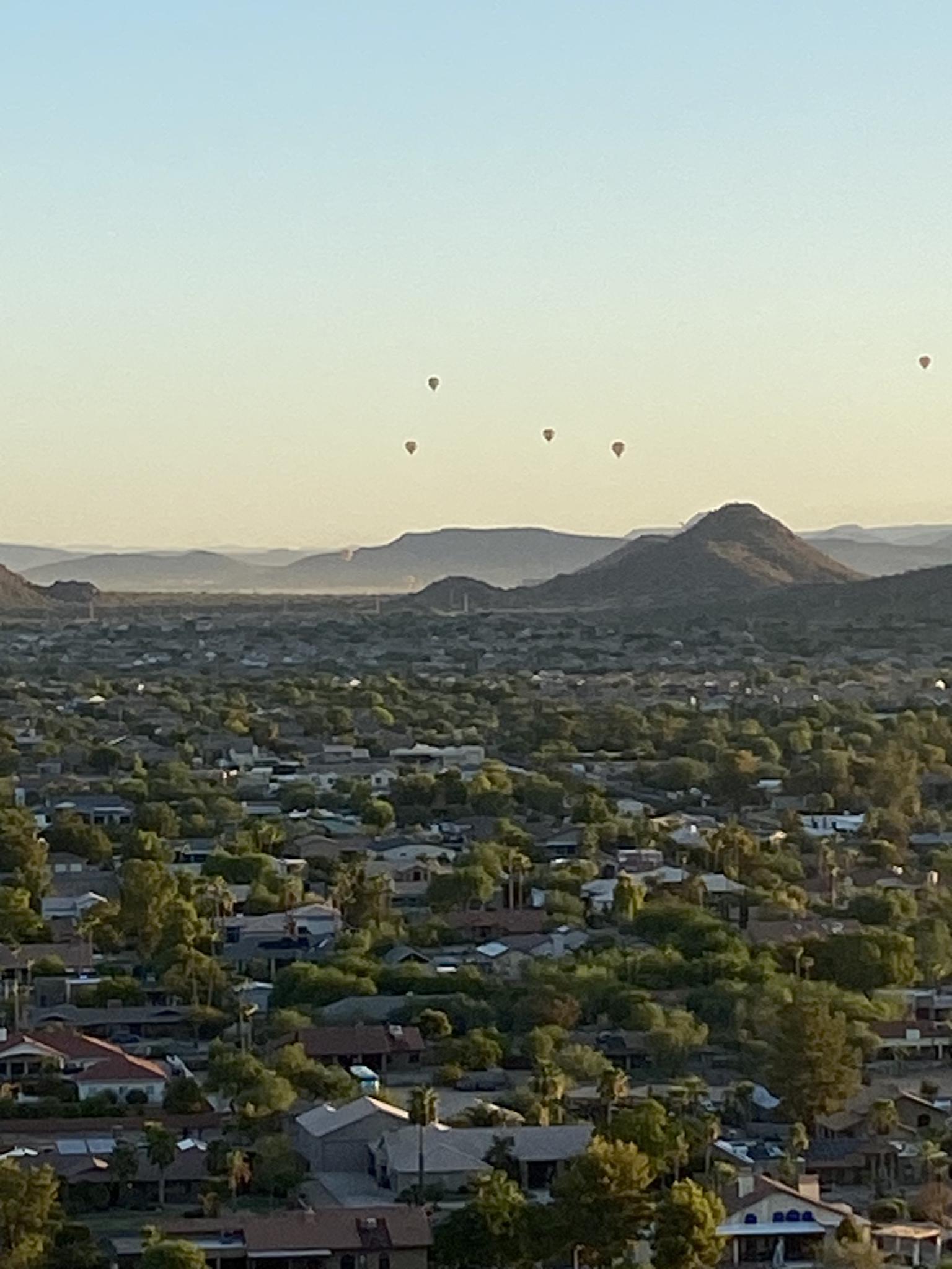 Aerial view of a city with mountains and several hot air balloons at sunrise.