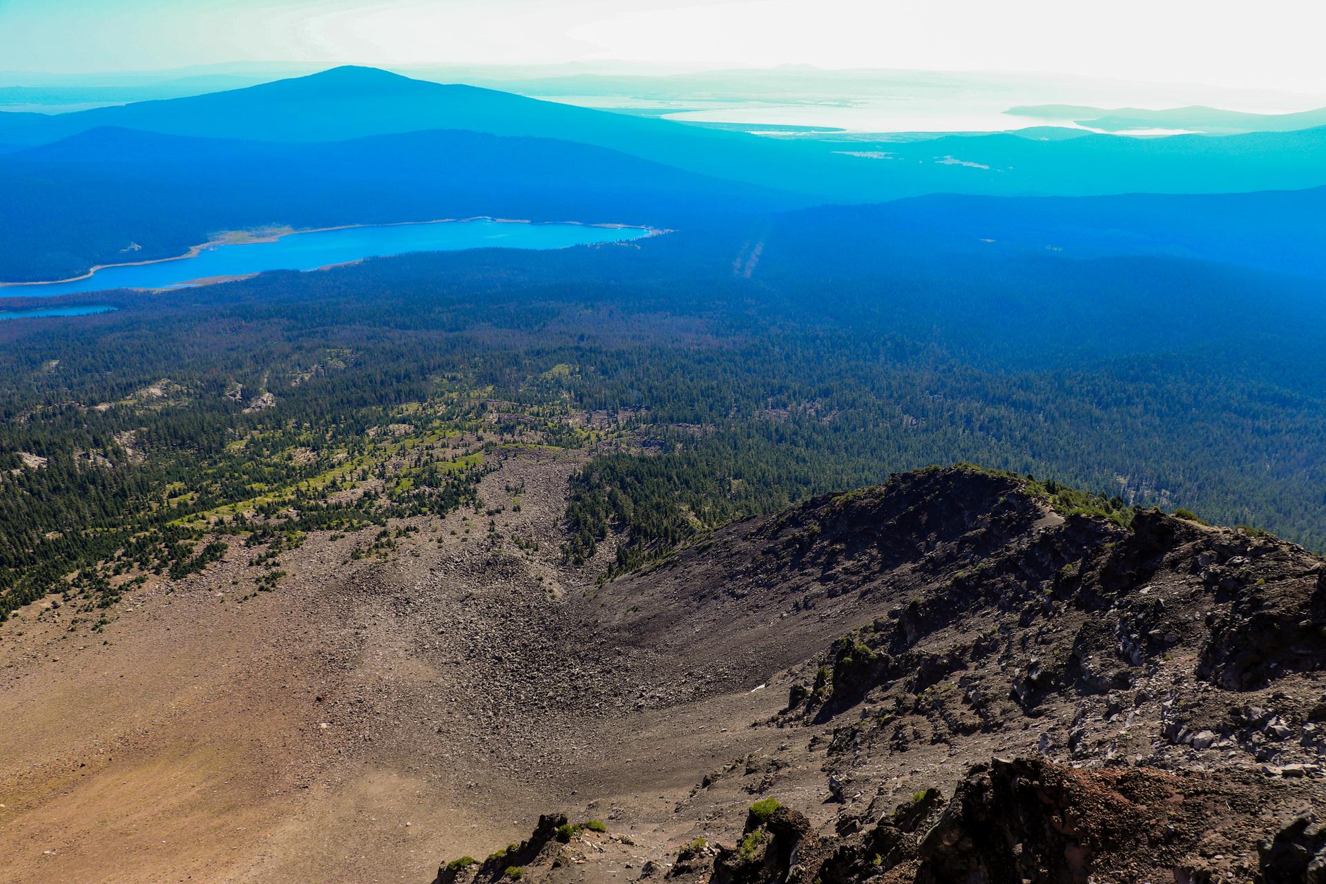 Aerial view of a rocky mountain slope, forest, and a large lake.