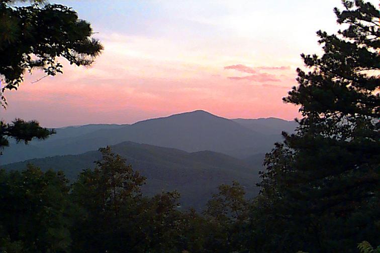 Silhouetted mountains and trees under a vibrant pink and purple sunset sky.