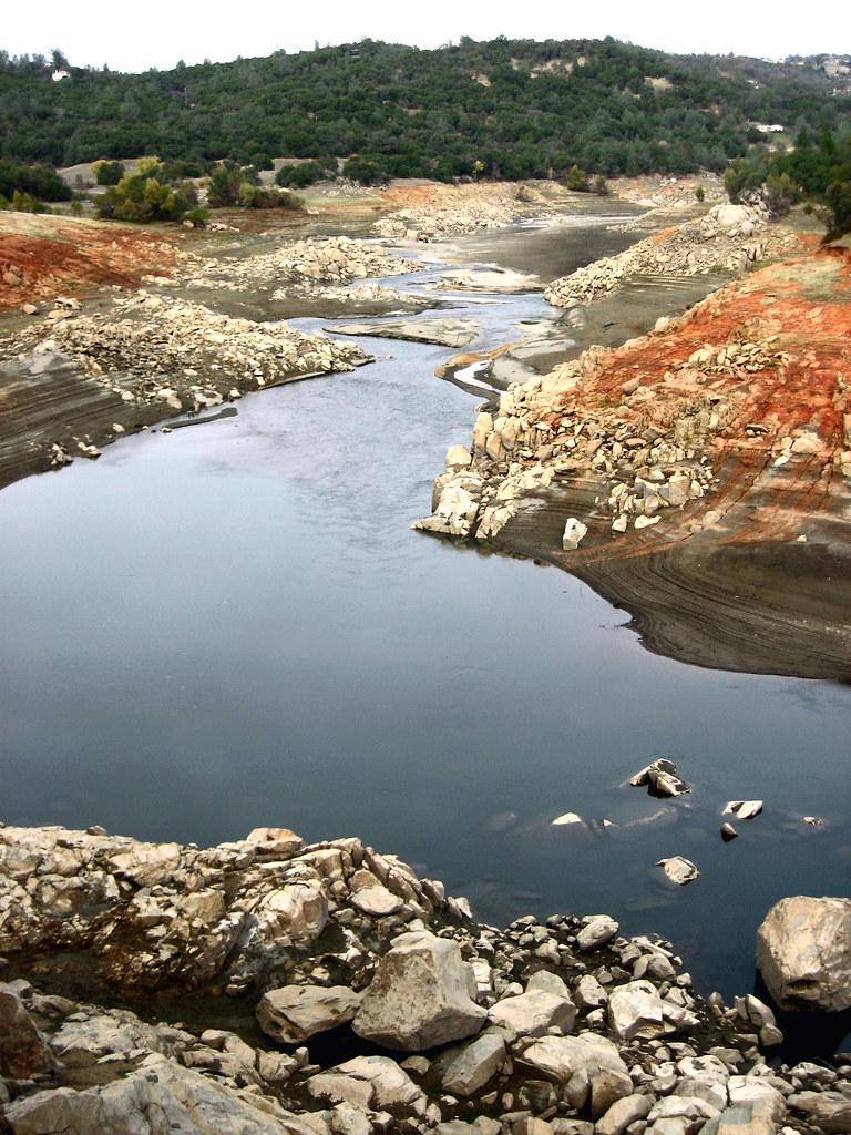 Low water in a rocky riverbed with exposed reddish-brown banks.