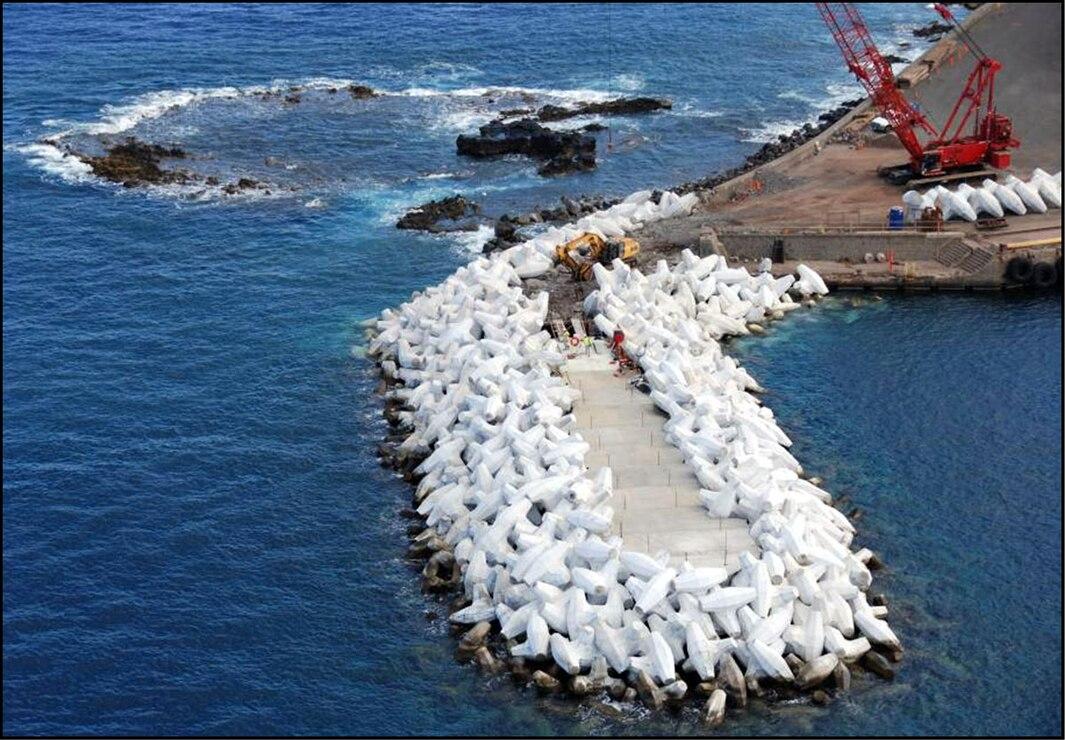 Construction of a white concrete breakwater extending into deep blue water.